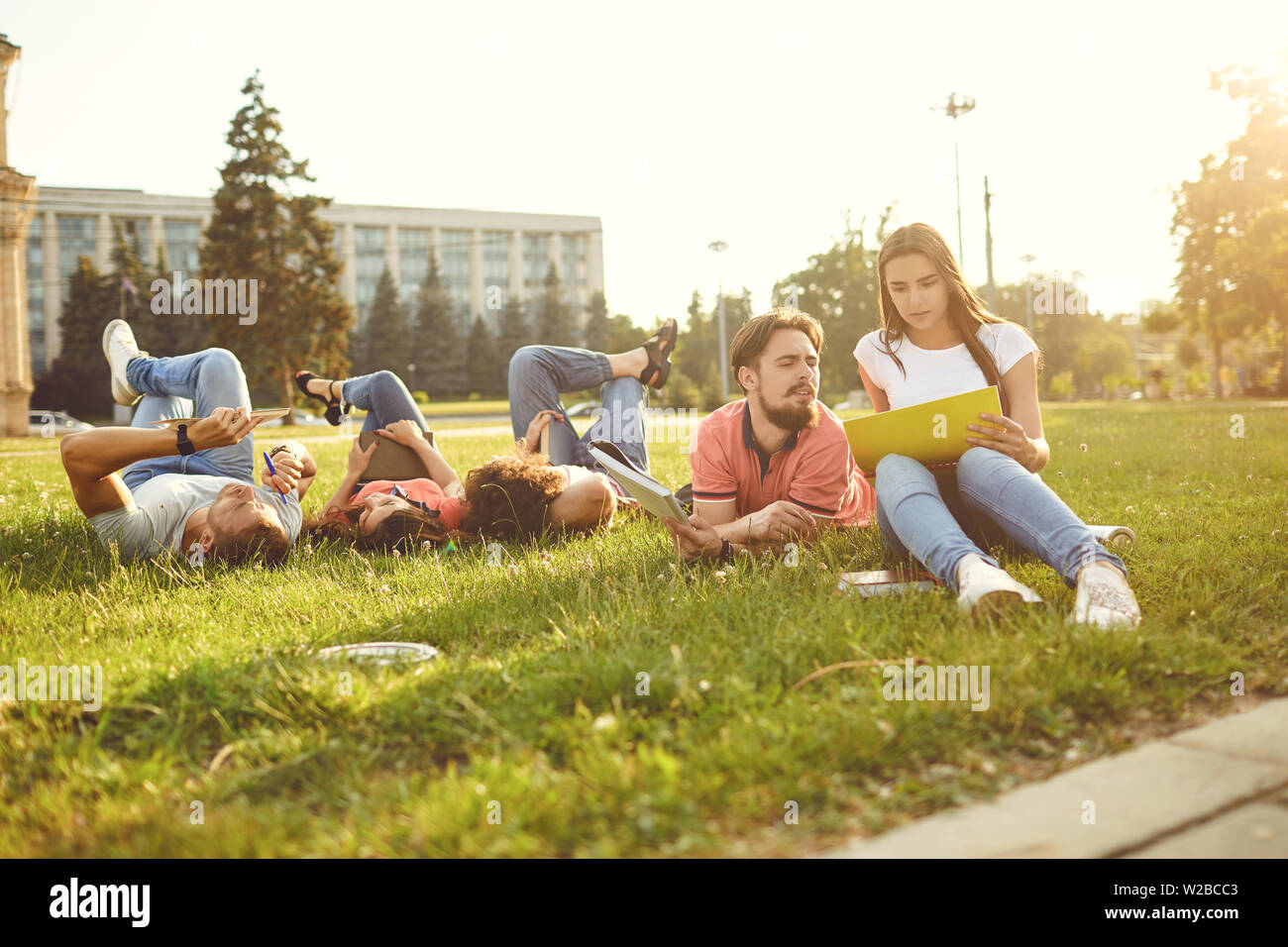I giovani sono di ridere mentre sdraiati sull'erba con libri nelle loro mani. Agli studenti di leggere i libri nel parco. Foto Stock
