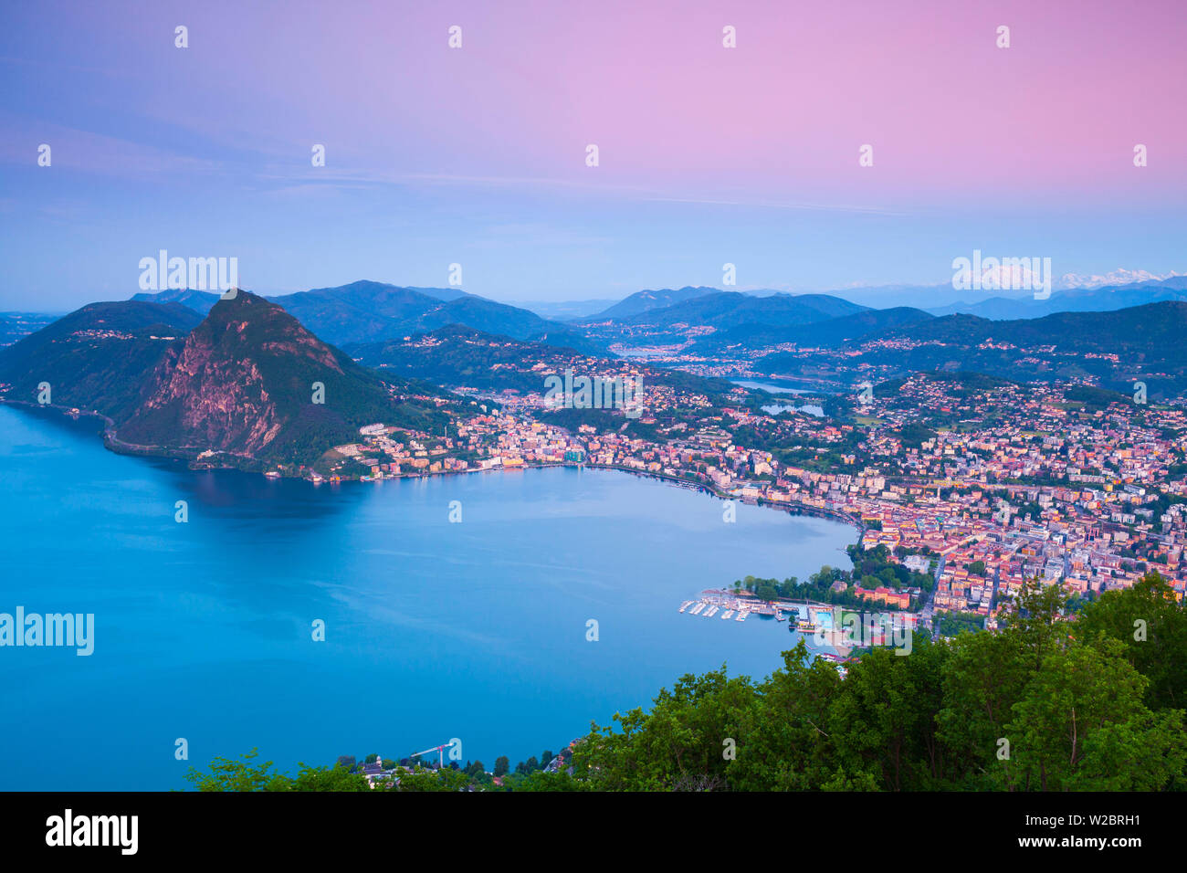 Vista in elevazione sopra Lugano dal Monte Bre illuminata di sunrise, Lugano, Lago di Lugano Ticino, Svizzera Foto Stock