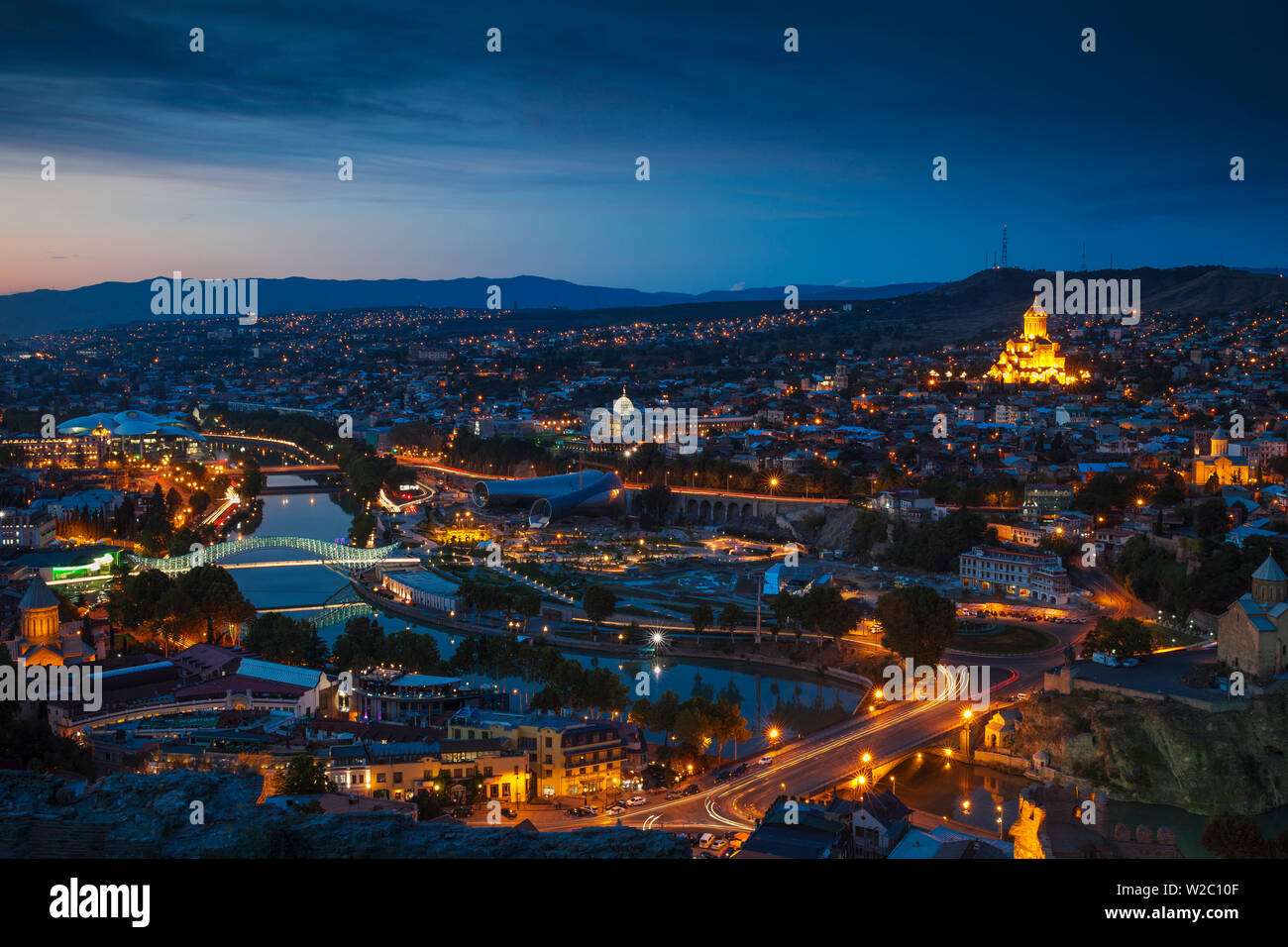 La Georgia, Tbilisi, vista di Tbilisi guardando verso il ponte di Metekhi e Chiesa, ponte di pace e il servizio pubblico edificio sulla destra - Rike Park il teatro e la sala delle esposizioni al di sotto del Palazzo Presidenziale e Tsminda Sameba Cattedrale (Santa trinità Cattedrale) Foto Stock