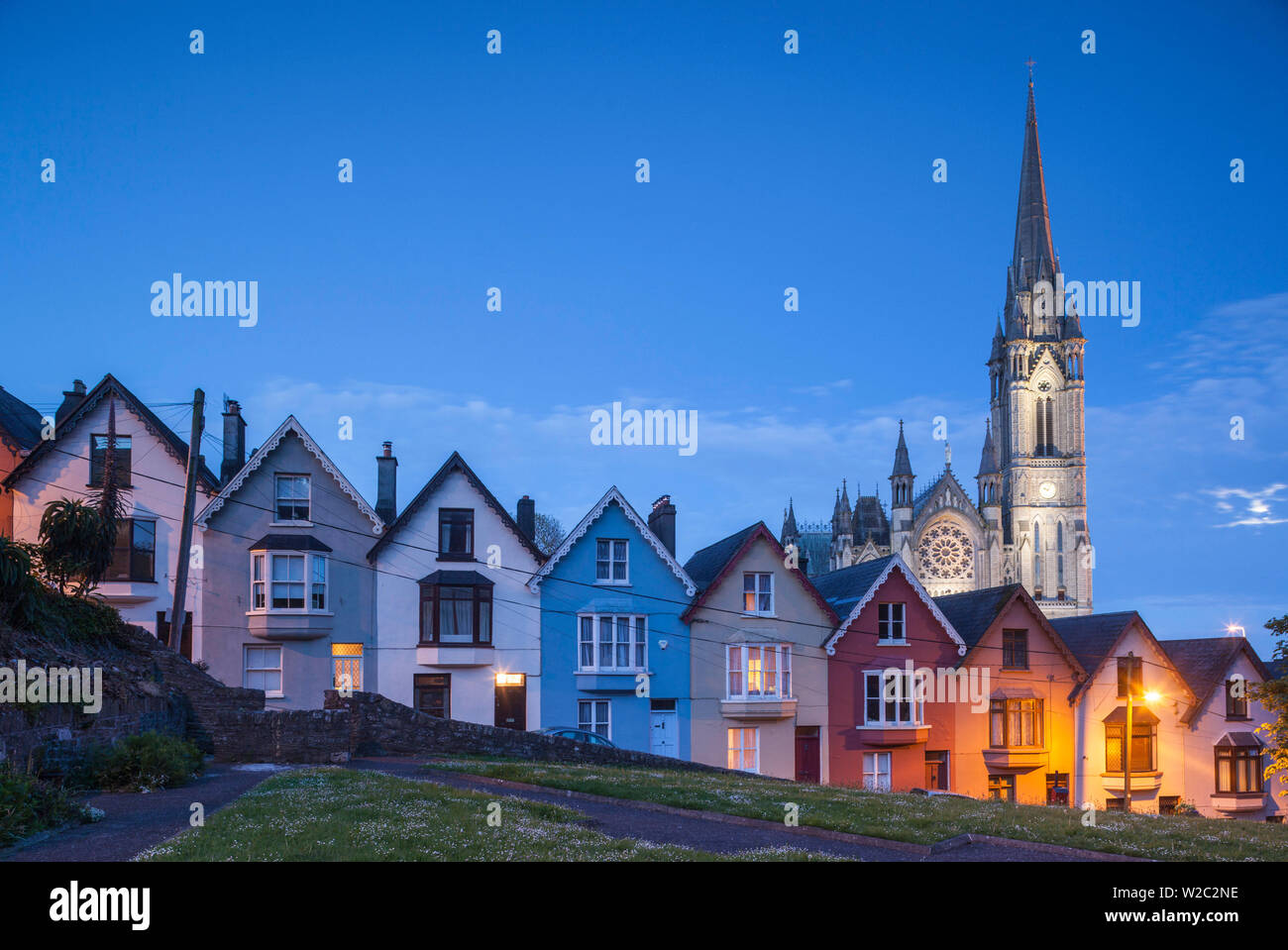 L'Irlanda, nella contea di Cork, Cobh, mazzo di carte hillside case e San Colman's Cathedral, crepuscolo Foto Stock