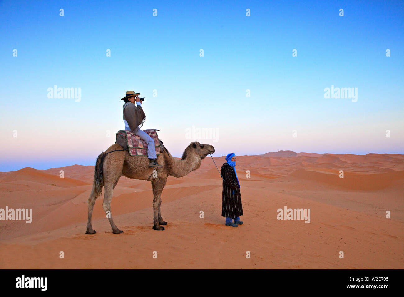 Turista nel deserto a dorso di cammello per fotografare, Merzouga, Marocco, Africa del Nord (MR) Foto Stock