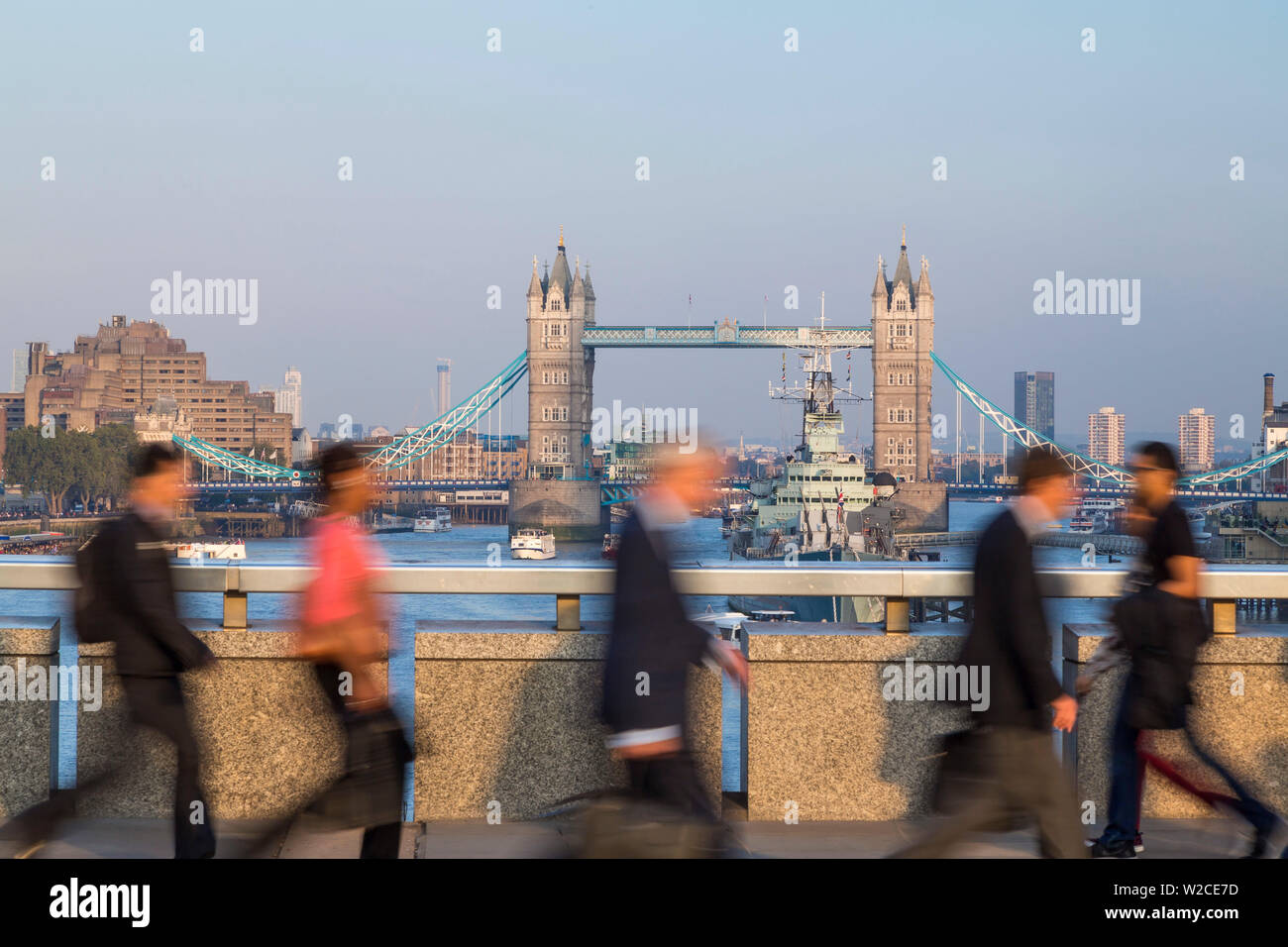 Pendolari attraversando il Ponte di Londra con il Tower Bridge dietro, London, Regno Unito Foto Stock