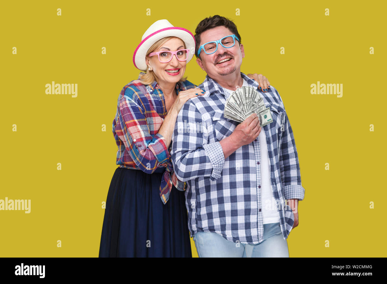 Felice famiglia benestante, adulto uomo e donna casual in camicia a scacchi pickaback permanente insieme, mantenendo la ventola del dollaro, sorriso toothy, guardando camer Foto Stock