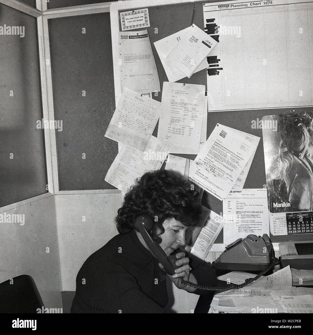 1974, storico, una femmina di lavorare in ufficio di un agente di viaggio, parlando al telefono, Inghilterra, Regno Unito. Foto Stock