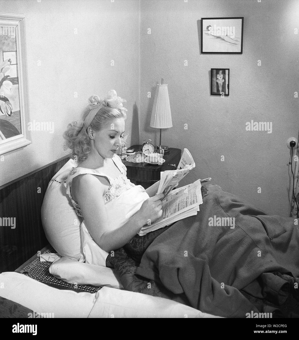 Donna di 1940s. Una giovane donna è sdraiato sul letto legge il giornale del mattino e beve caffè. La Svezia 1948. Kristoffersson ref un61-3 Foto Stock