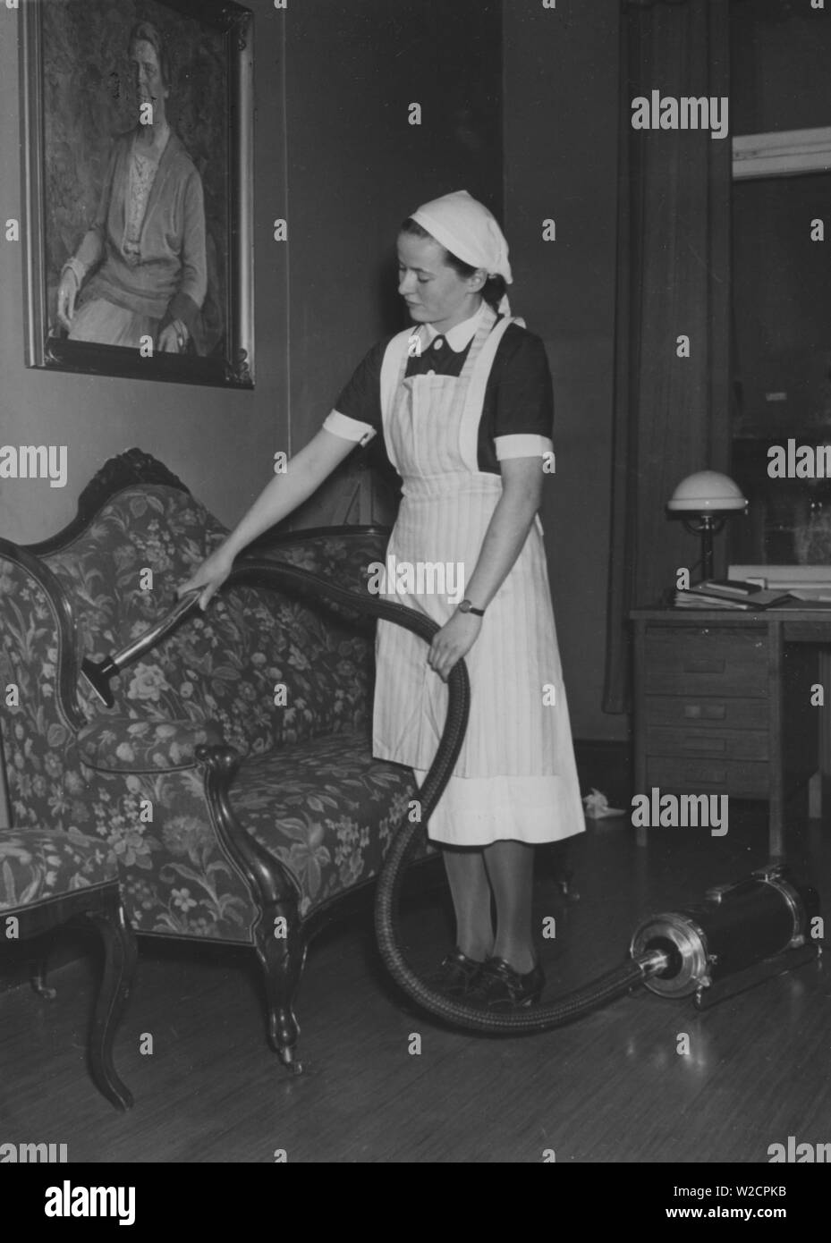 Aspirapolvere in 1940s. Una giovane schiava è di aspirare il lettino accuratamente. Ella è vestito con il suo bianco abito da lavoro. La Svezia 1940s Foto Stock