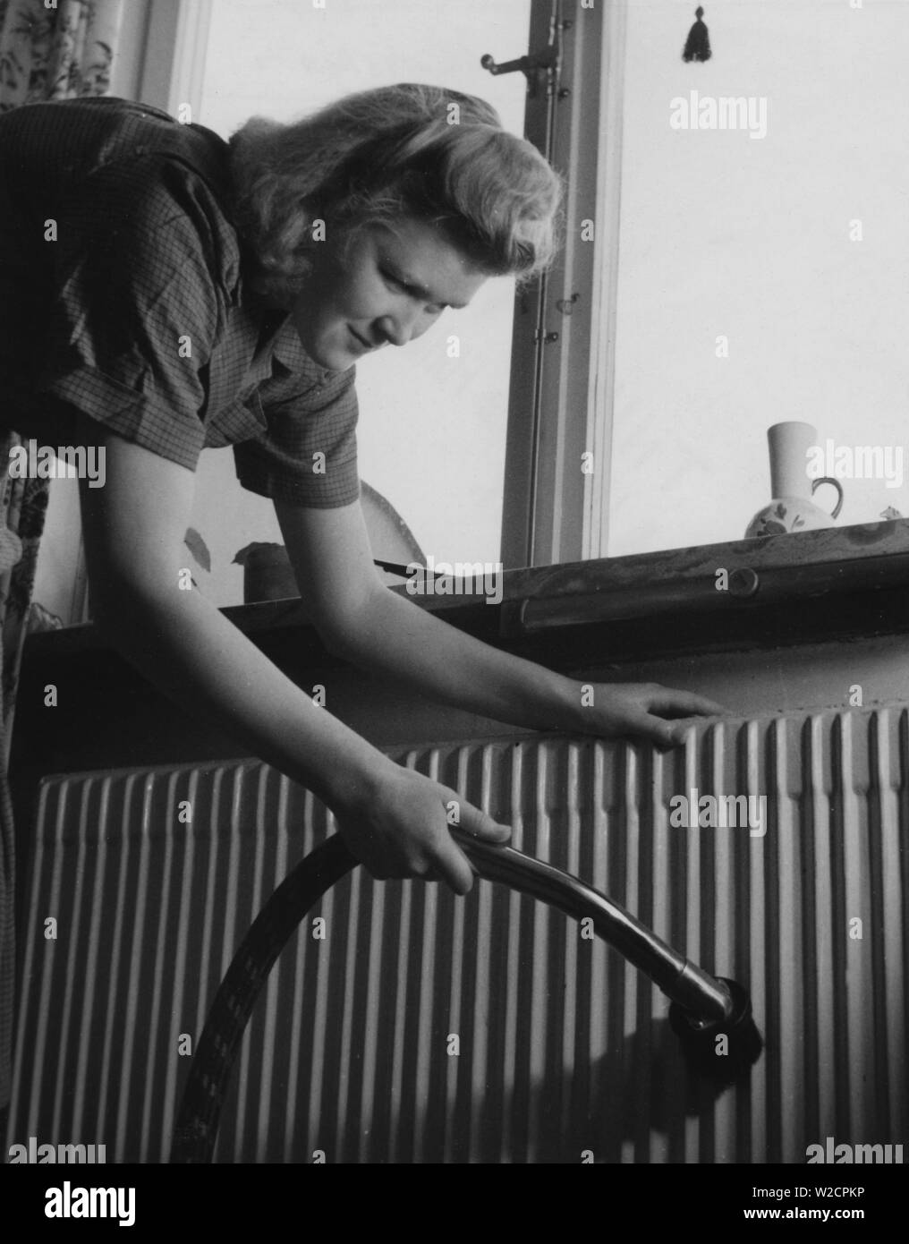 Giornata di pulizia nel 1940s. Una giovane donna è la pulizia il suo appartamento e l'aspirazione del radiatore sotto la finestra. La Svezia 1948 Foto Stock