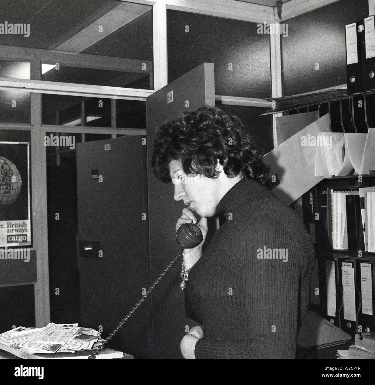 1974, storico, una femmina di lavorare in ufficio di un agente di viaggio, parlando al telefono, Inghilterra, Regno Unito. Foto Stock