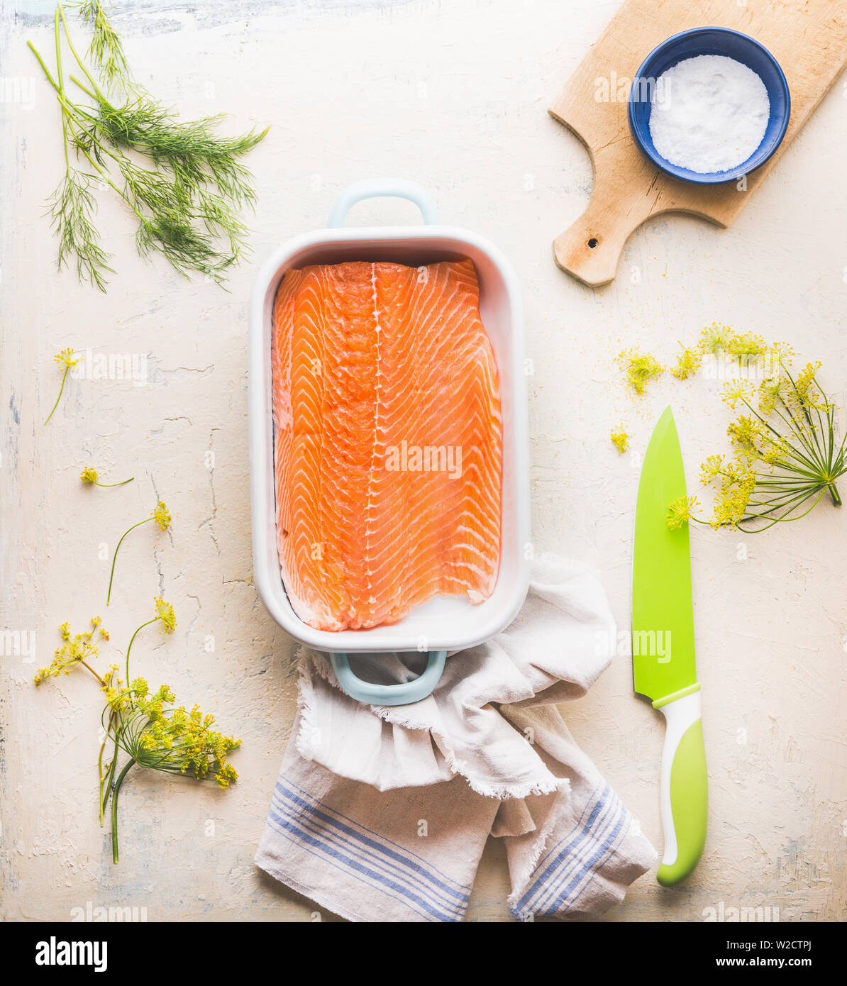 La cottura di preparazione del salmone. Materie filetto di salmone con aneto in una casseruola su sfondo bianco con tagliere e coltello da cucina, vista dall'alto. Se sano Foto Stock
