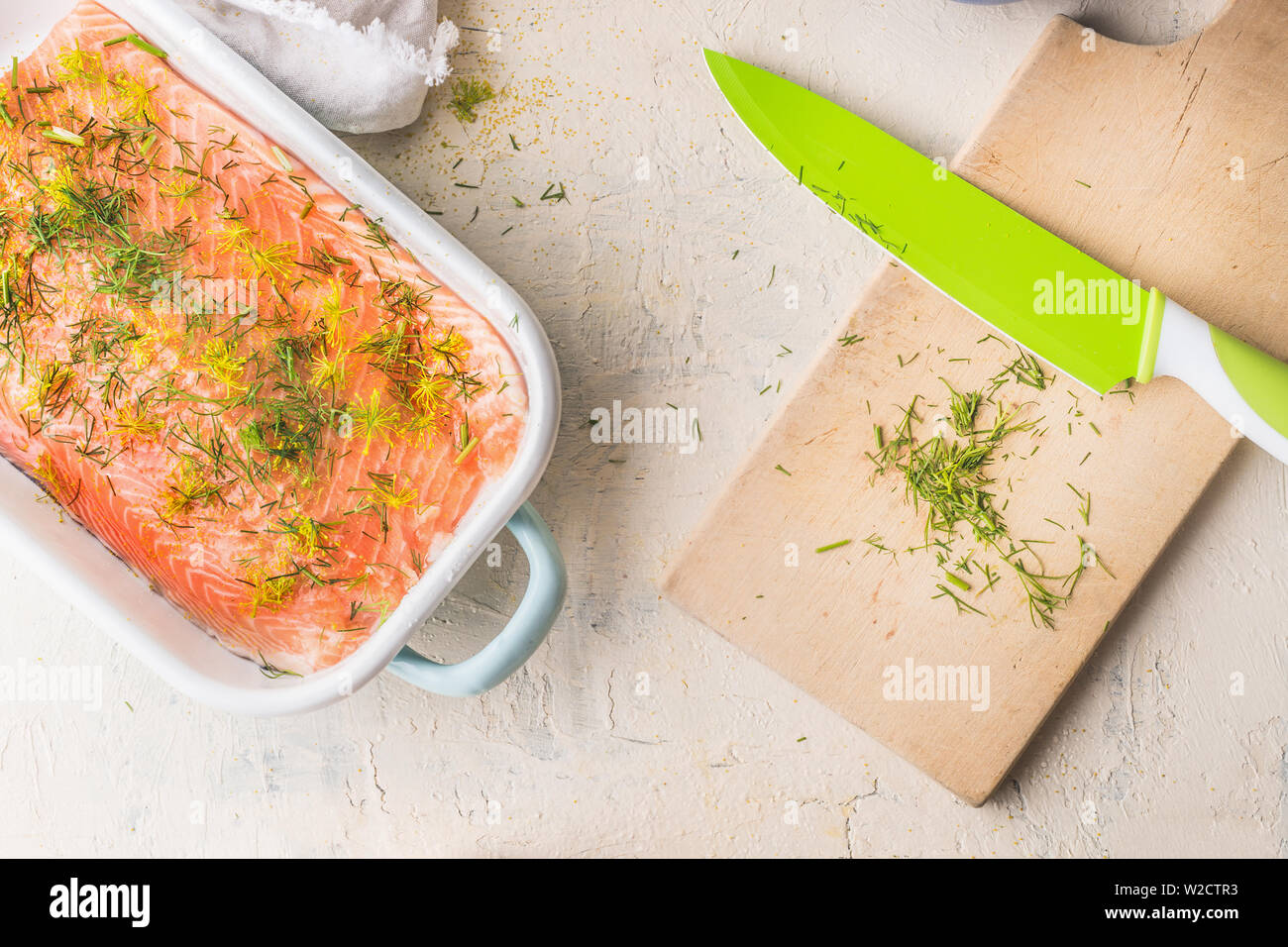 Materie filetto di salmone con aneto in casseruola di bianco su sfondo chiaro con tagliere e coltello da cucina, vista dall'alto. Un sano concetto di frutti di mare. La dieta alimentare. Foto Stock