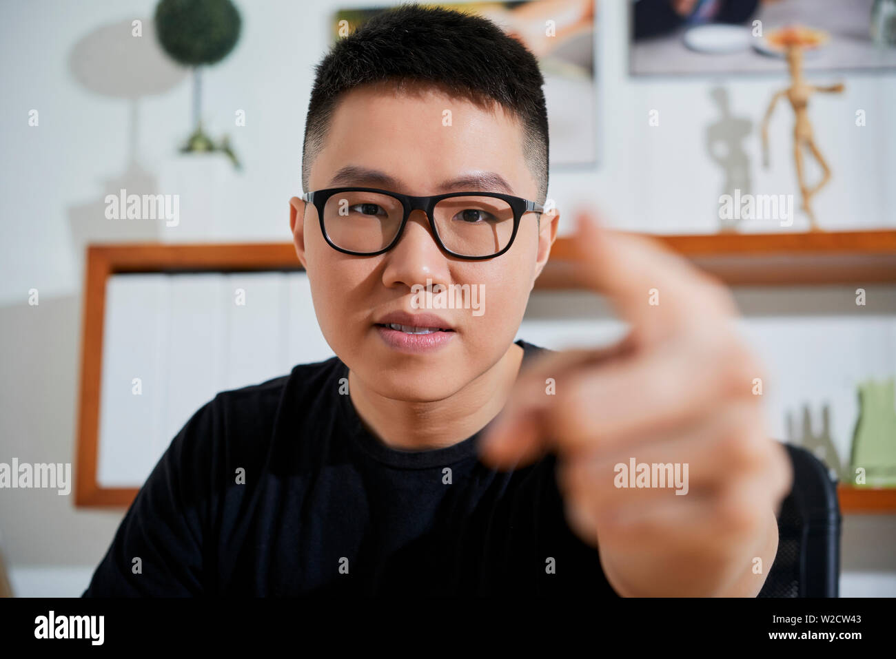 Ritratto di giovane uomo asiatico indossando occhiali puntando alla fotocamera e scegliendo lei mentre è seduto in ufficio Foto Stock