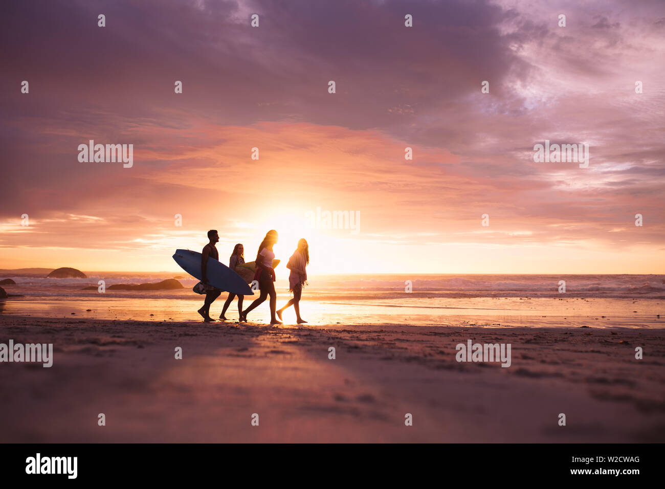 La gente camminare sulla spiaggia durante il tramonto. Coppia in vacanza passeggiate sulla spiaggia che trasportano le tavole da surf. Foto Stock