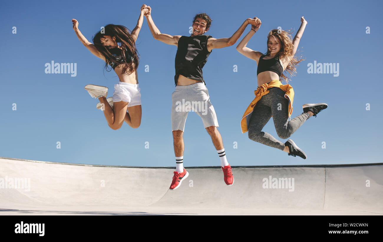 Tre giovani persone che saltano all'esterno. Gruppo di amici in allegro su un giorno d'estate. Foto Stock