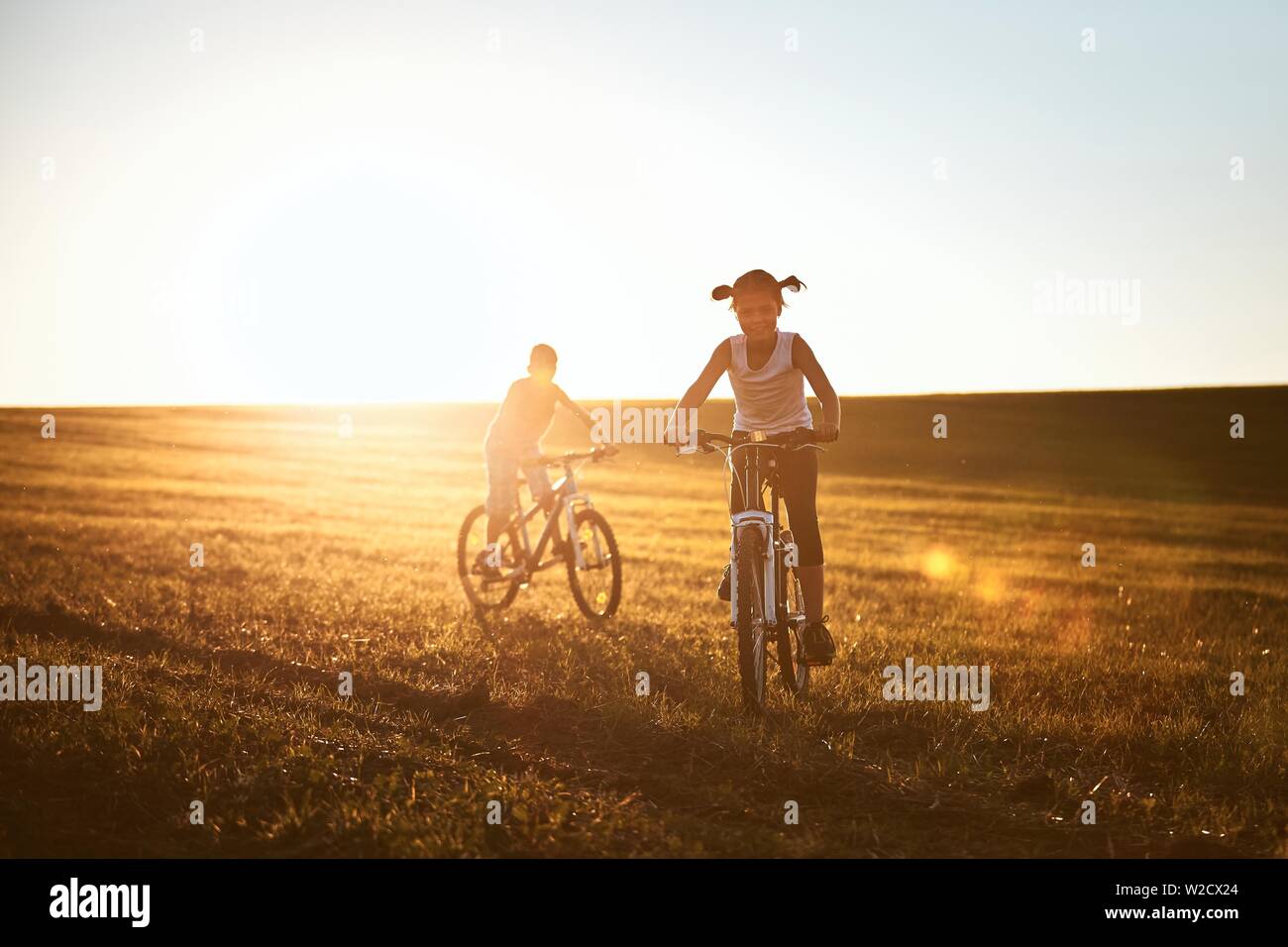 Ragazzo e una ragazza godendo in bicicletta sul prato. Estate viaggio in campagna al tramonto. Foto Stock