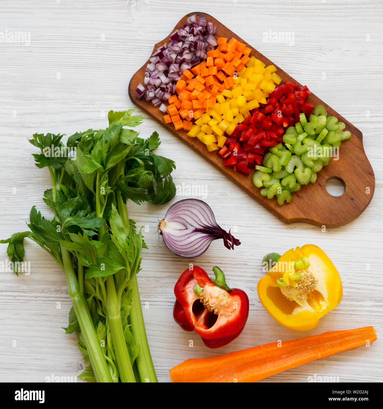 Da sopra, un trito di verdure fresche (carota, sedano, cipolla rossa, peperoni rossi e gialli) disposti sul bordo di taglio su un bianco sullo sfondo di legno. Overh Foto Stock