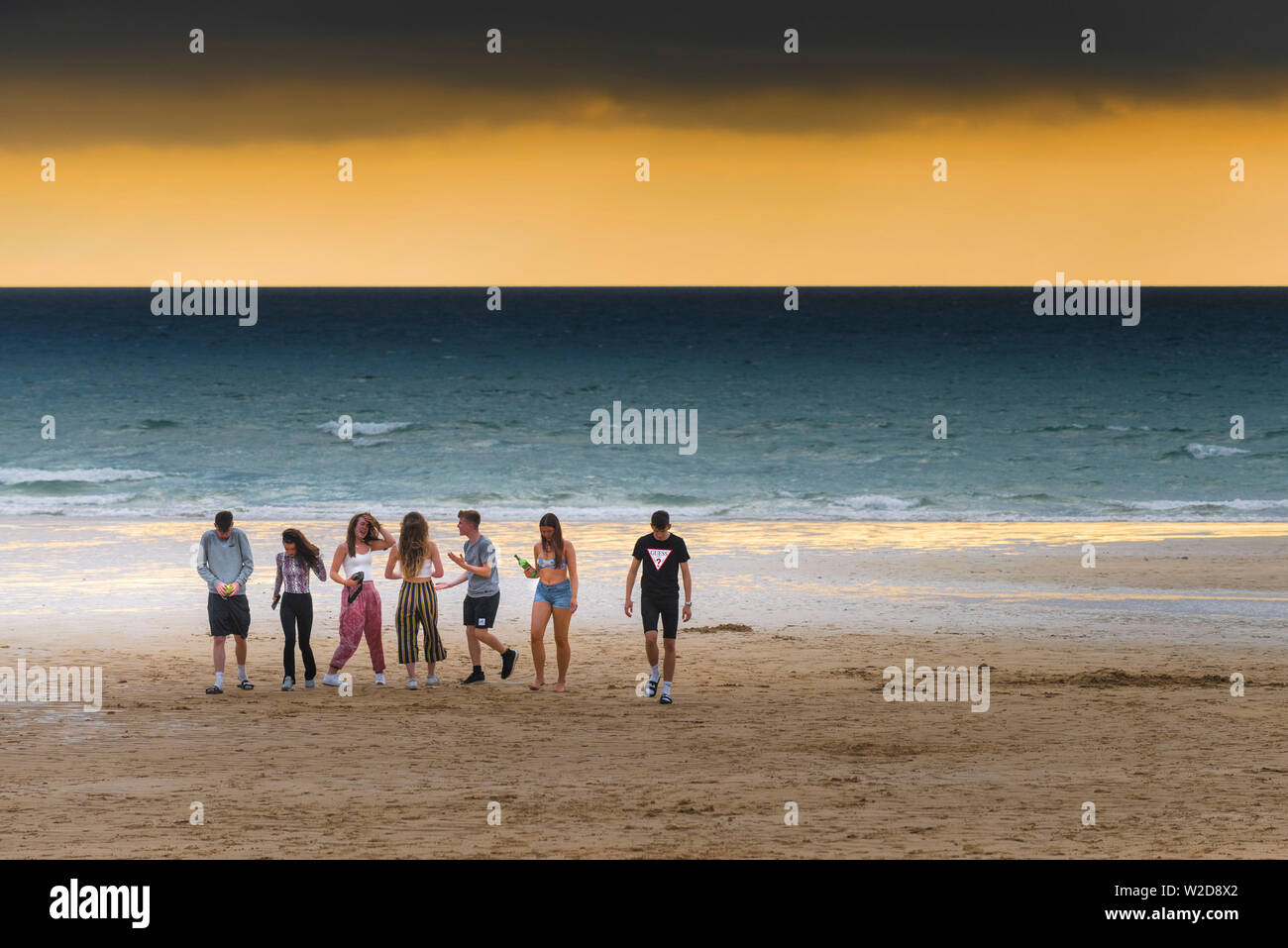 Un gruppo di adolescenti appendere fuori su Fistral Beach durante un tramonto spettacolare a Newquay in Cornovaglia. Foto Stock