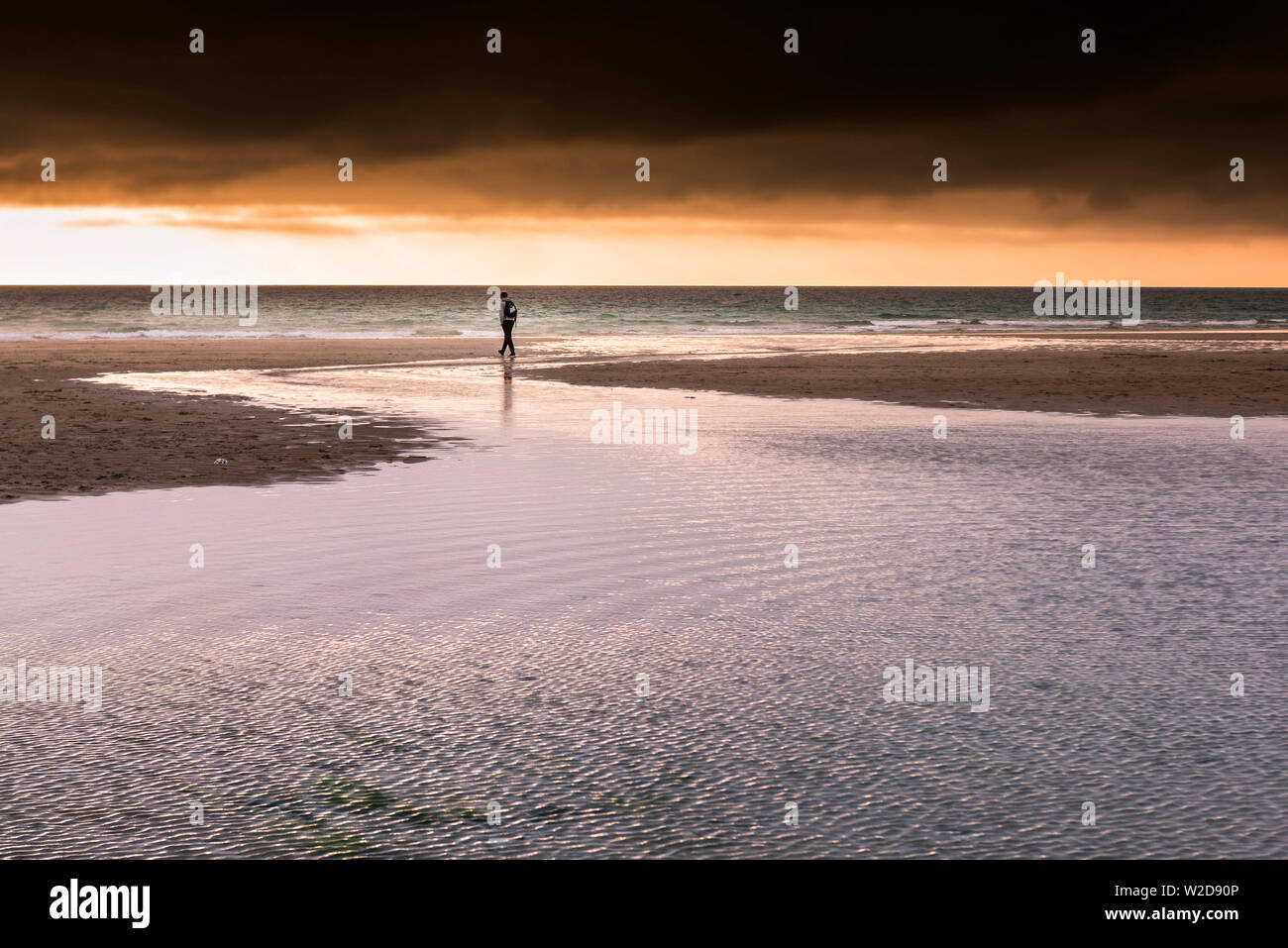 Un ragazzo adolescente camminare da sole al tramonto attraverso Fistral Beach in Newquay in Cornovaglia. Foto Stock