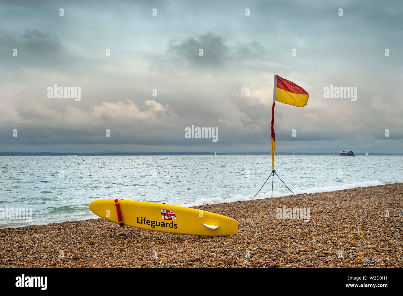 Bagnino RNLI scheda gialla e rossa e gialla sono sicuro bandiera su una spiaggia di ciottoli. Foto Stock