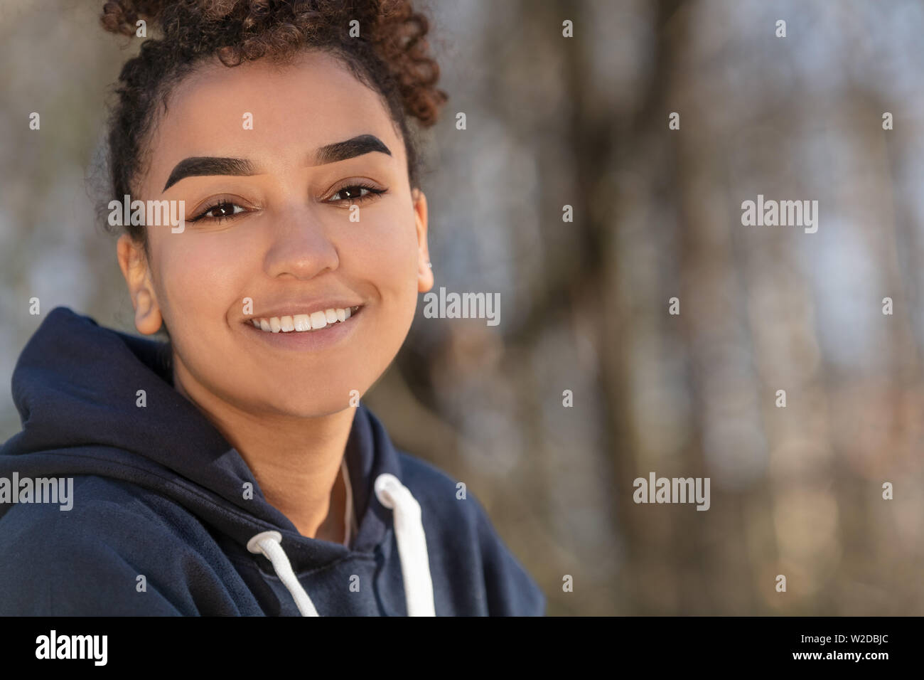 Outdoor ritratto della bella felice razza mista biracial americano africano ragazza adolescente femmine giovane donna sorridente con denti perfetti indossando un blu ho Foto Stock