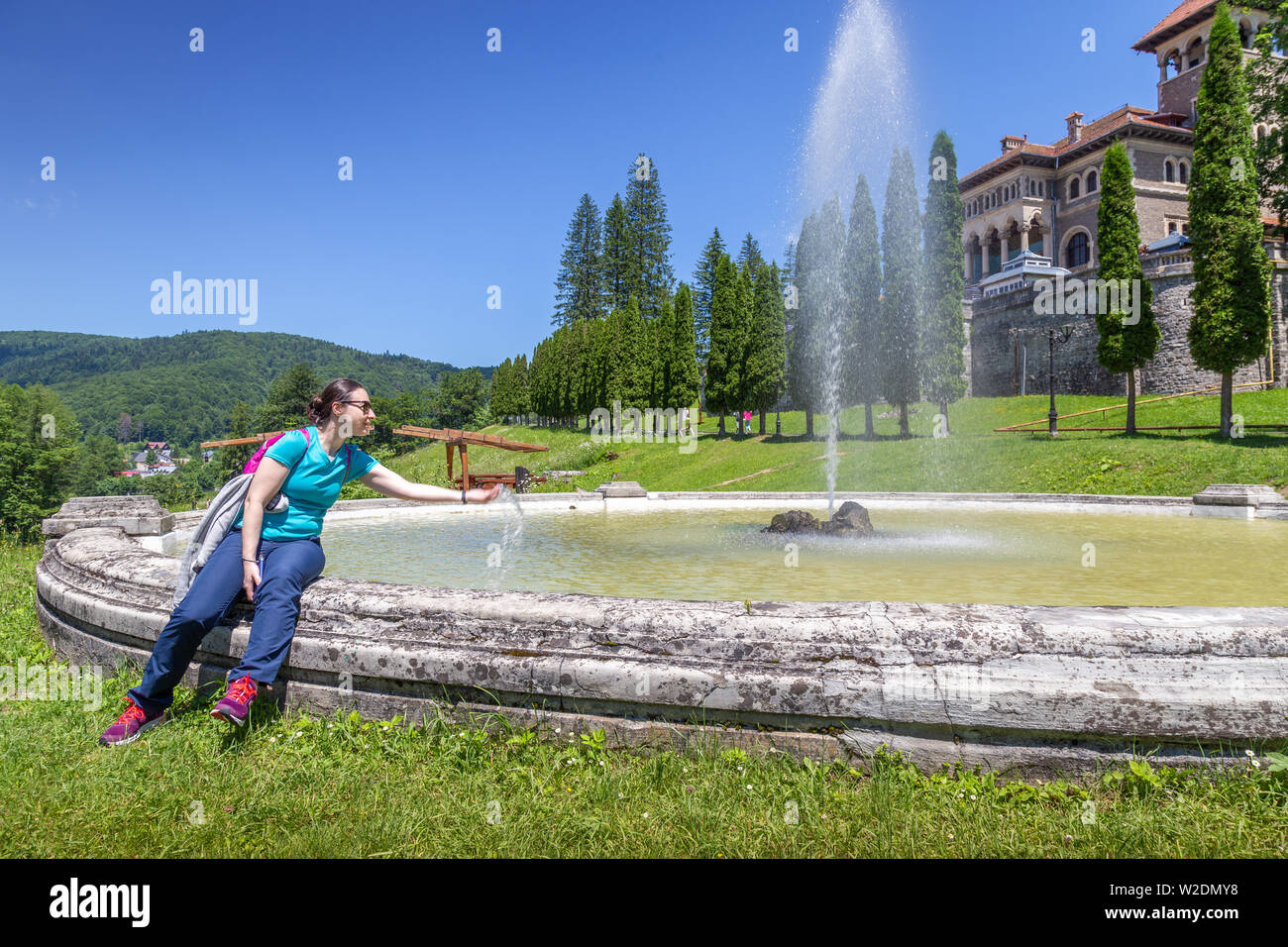 Giovane donna rinfrescante nella fontana nella parte anteriore del castello Cantacuzino in Busteni, Romania Foto Stock