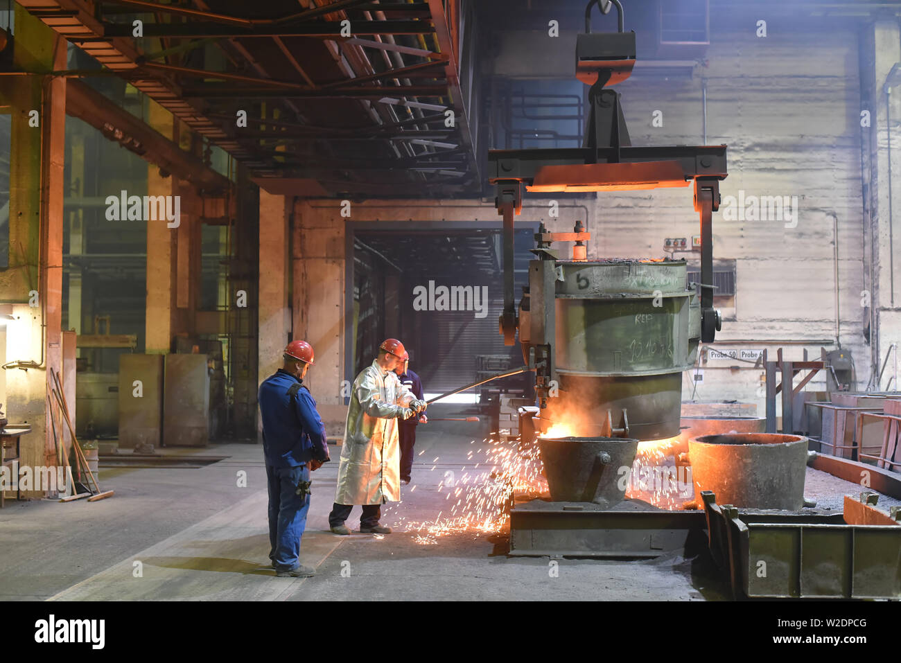 I lavoratori di attrezzature di protezione in una fonderia durante la produzione di componenti in acciaio - sul posto di lavoro in fabbrica industriale Foto Stock