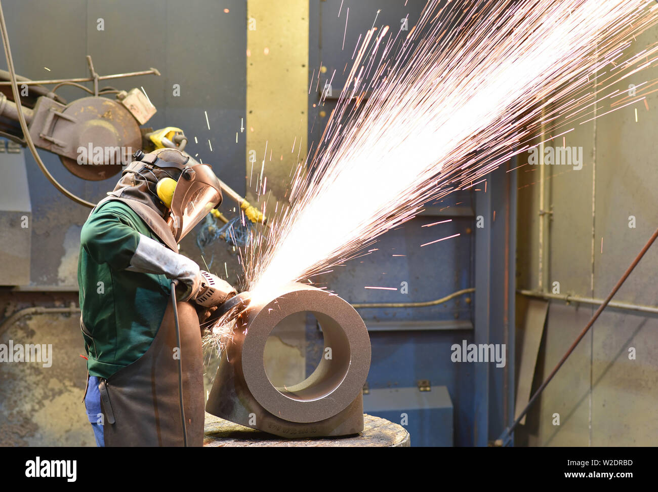 I lavoratori di attrezzature di protezione in un lavoro di fonderia su un pezzo fuso con una macchina di macinazione sul posto di lavoro Foto Stock