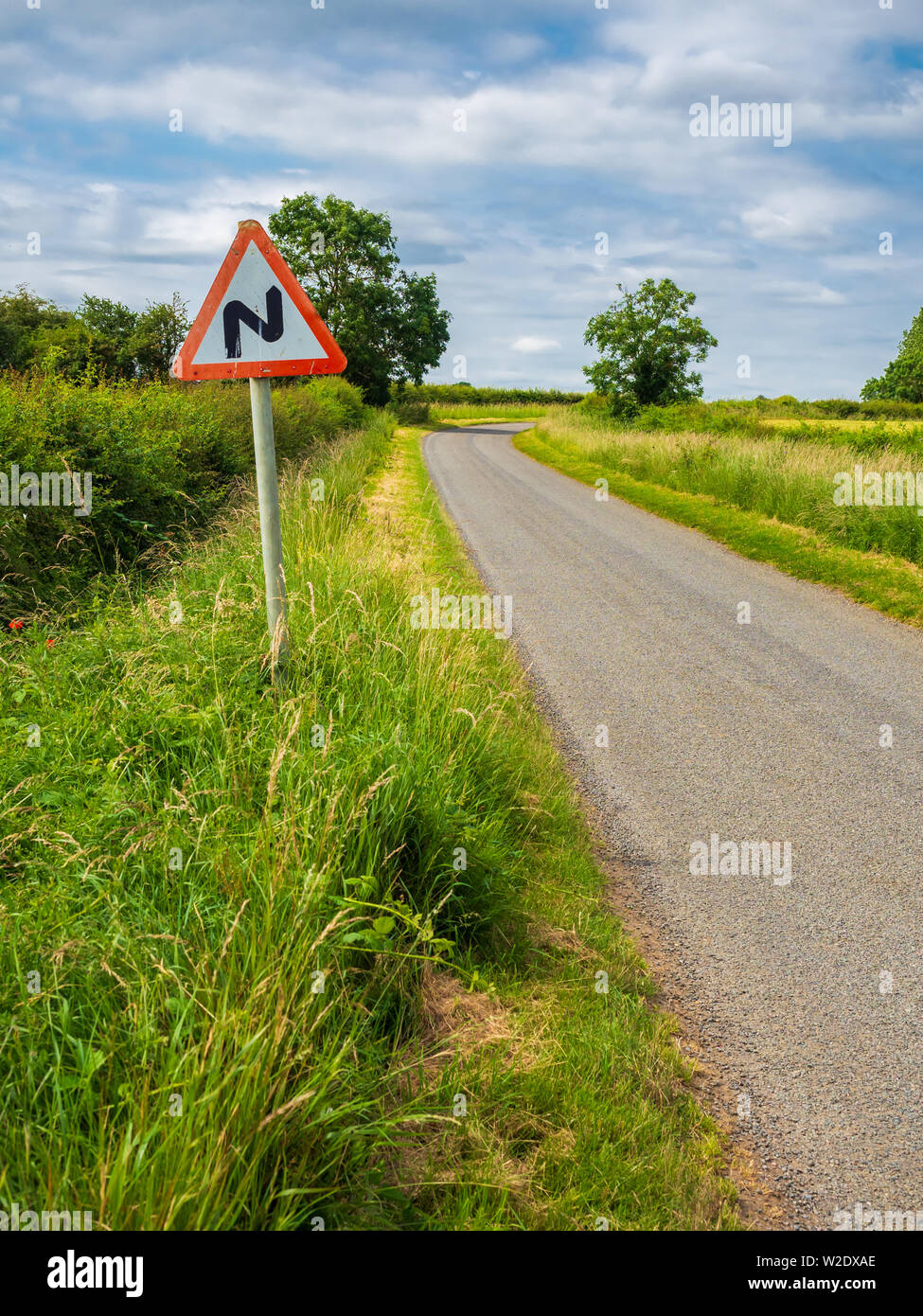 Strada tortuosa davanti a zig zag segno a lato di una singola traccia country road Foto Stock