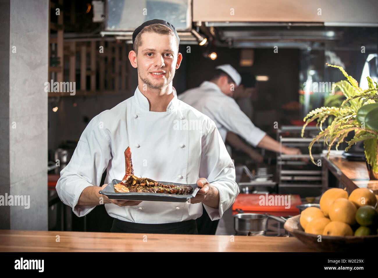 Sorridente maschio bello cuocere tenendo piatto in cucina del ristorante Foto Stock