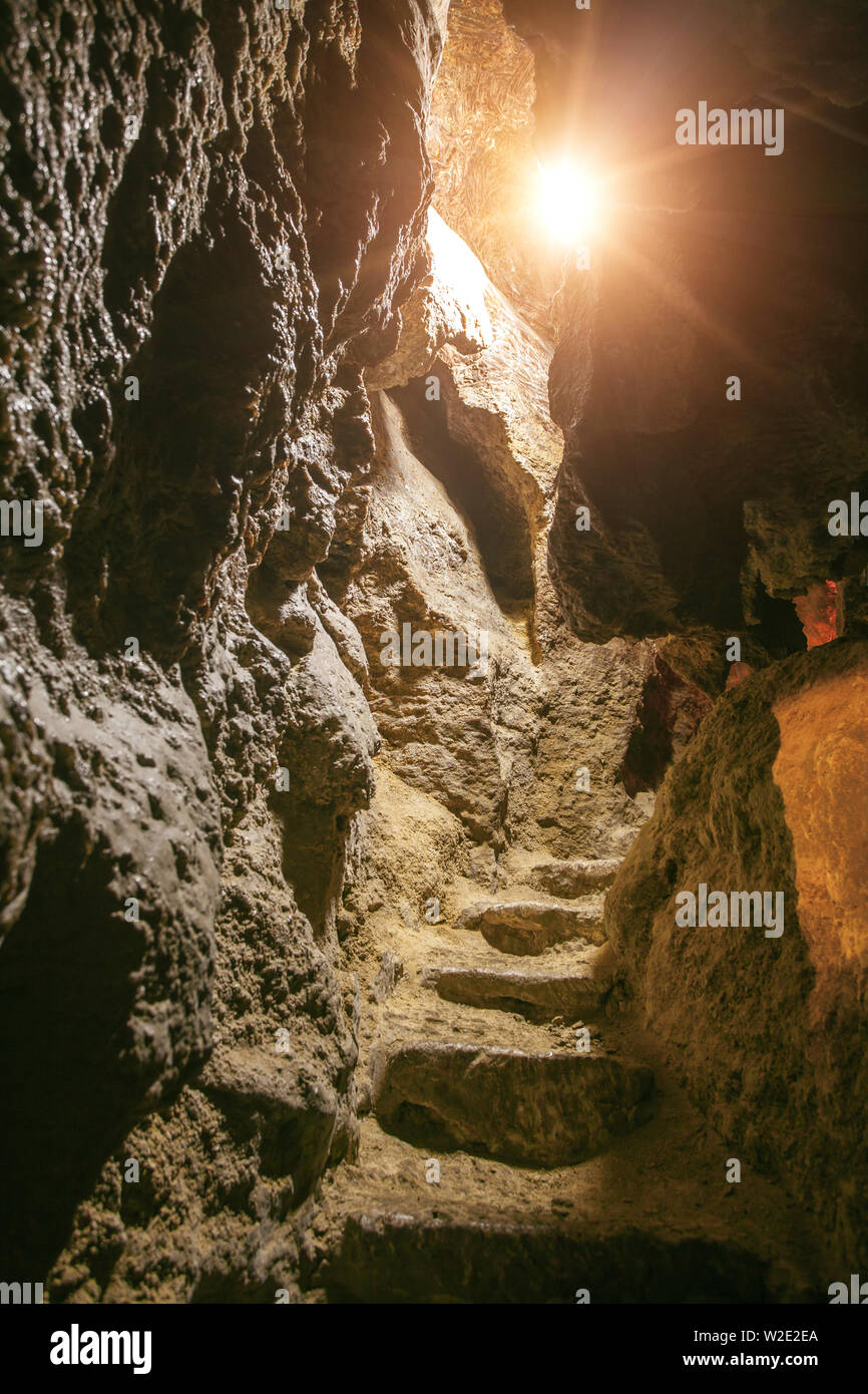 Guardando all'interno della grotta di roccia. scale nella grotta di roccia con la luce solare Foto Stock