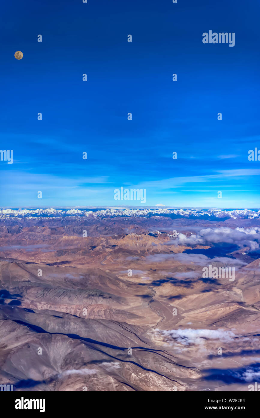 Luna piena sopra le montagne brulle della Zanskar gamma di Himalaya interna, India. Preso da un piano su un inizio di luglio mattina. Orientamento verticale. Foto Stock