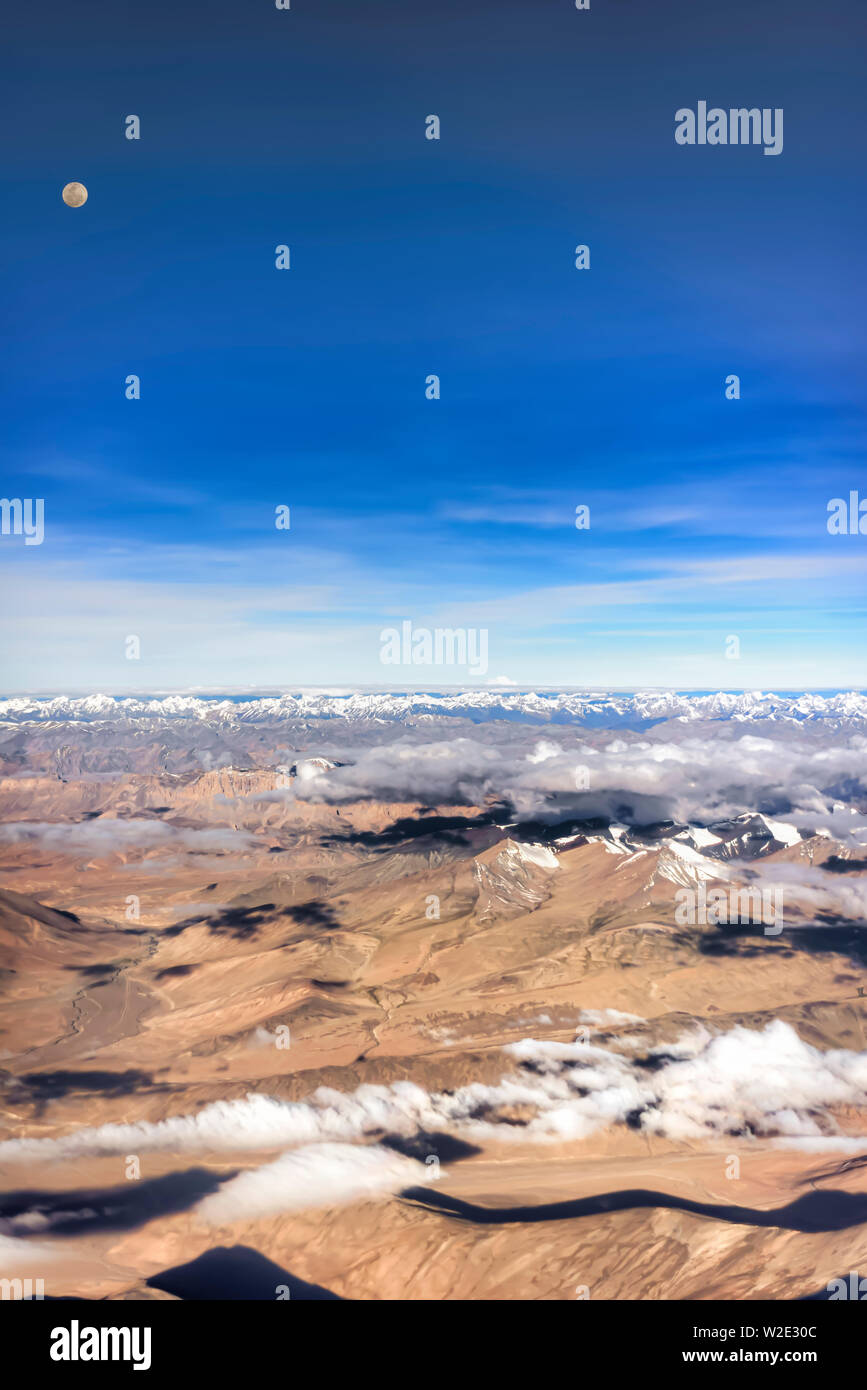 Luna piena sopra le montagne brulle della Zanskar gamma di Himalaya interna, India. Preso da un piano su un inizio di luglio mattina. Orientamento verticale. Foto Stock