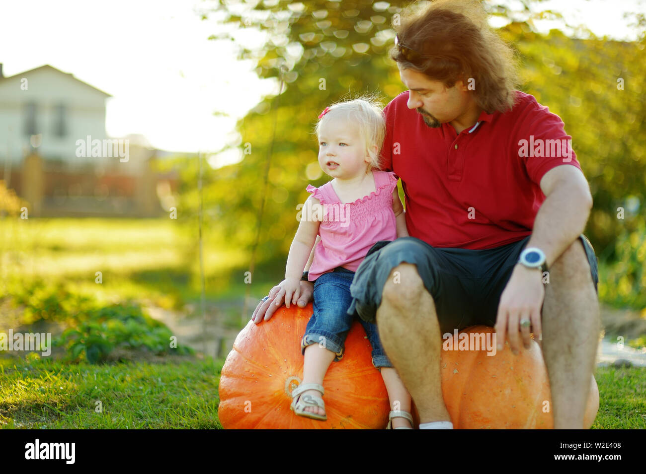 Il Toddler ragazza e il suo papà seduto su un enorme varietà di zucche su una zucca patch. Bambini Raccolta zucche di country farm nelle calde giornate d'autunno. Tempo per la famiglia a Thanksg Foto Stock