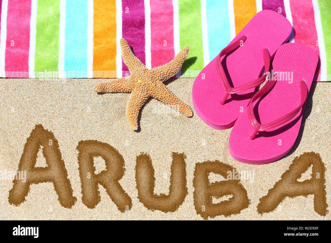 Aruba beach concetto di viaggio. ARUBA scritto in sabbia con acqua vicino al telo da spiaggia, estate sandali e stelle marine. Estate e sole vacanza vacanze. Foto Stock