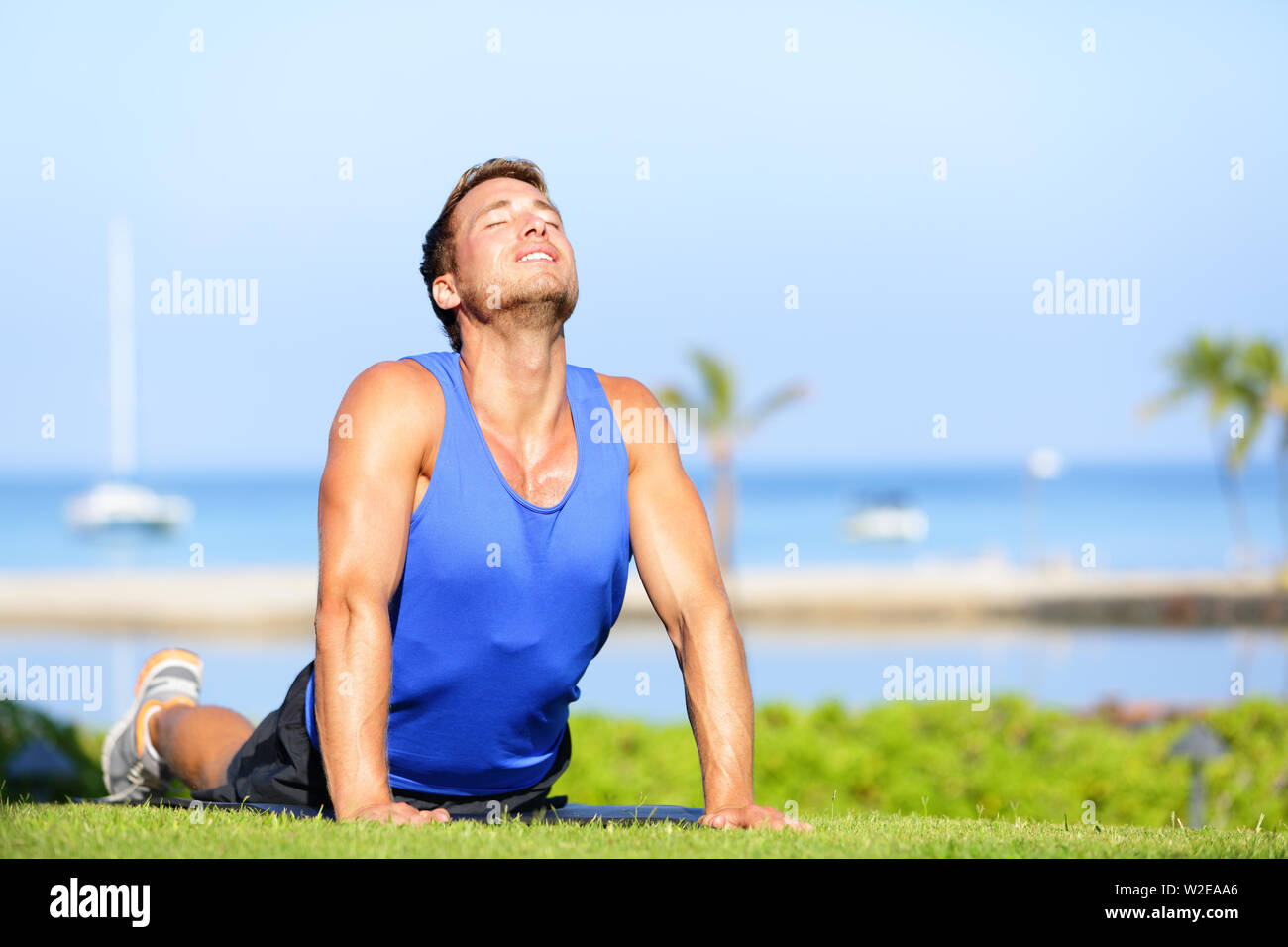 Yoga Fitness uomo in cobra pongono abs di stiramento dei muscoli dello stomaco. Montare maschio modello sportivo facendo stretching esercizio all'aperto in estate sull'erba. Bel giovane maschio di istruttore sportivo. Foto Stock