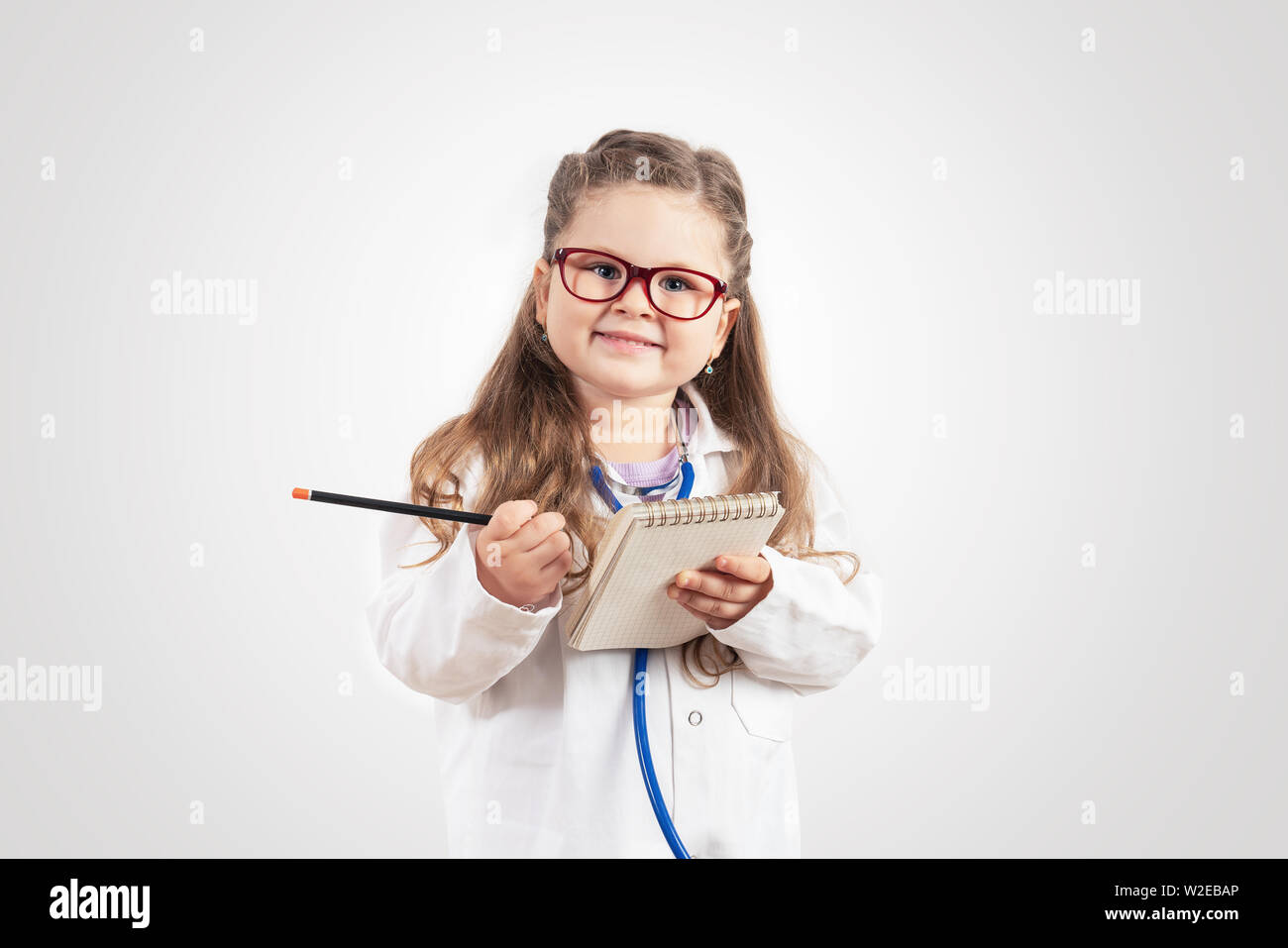 Poco carino ragazza in costume medico tenendo sthetoscope sulla lavagna Foto Stock