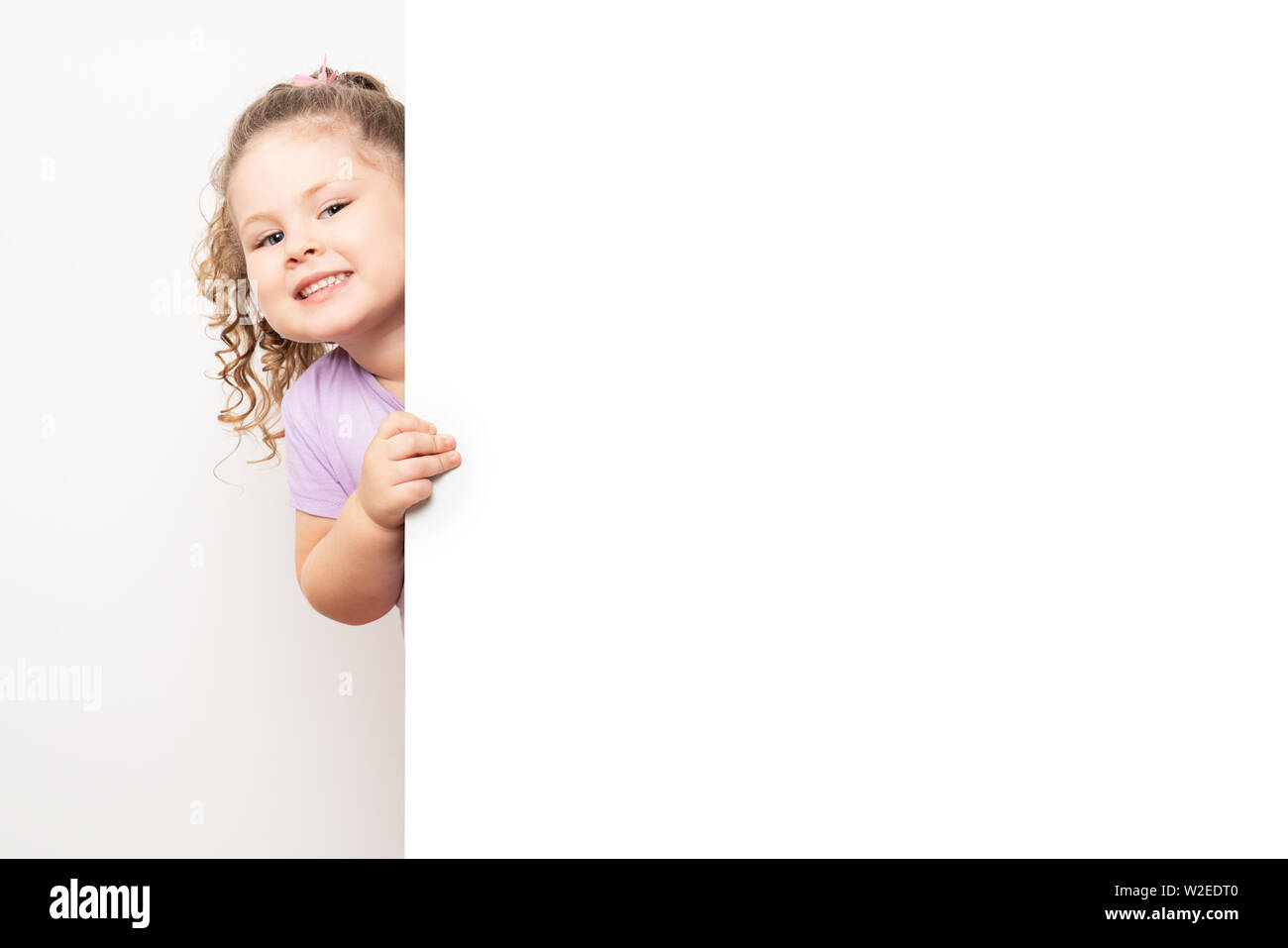 Sorridente dagli occhi blu bambina spiata dietro un pannello bianco. Foto Stock