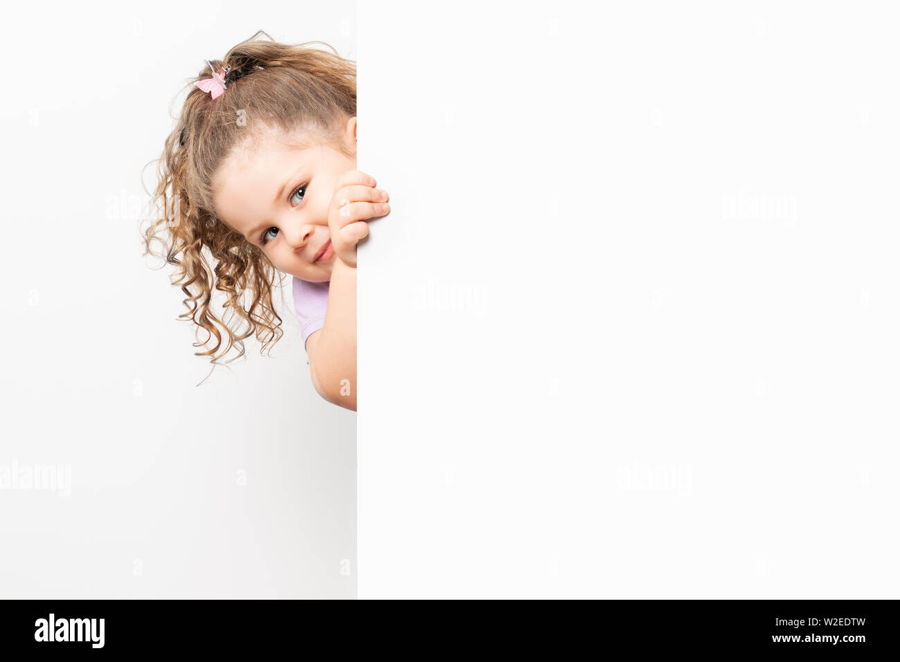 Sorridente dagli occhi blu bambina spiata dietro un pannello bianco. Foto Stock