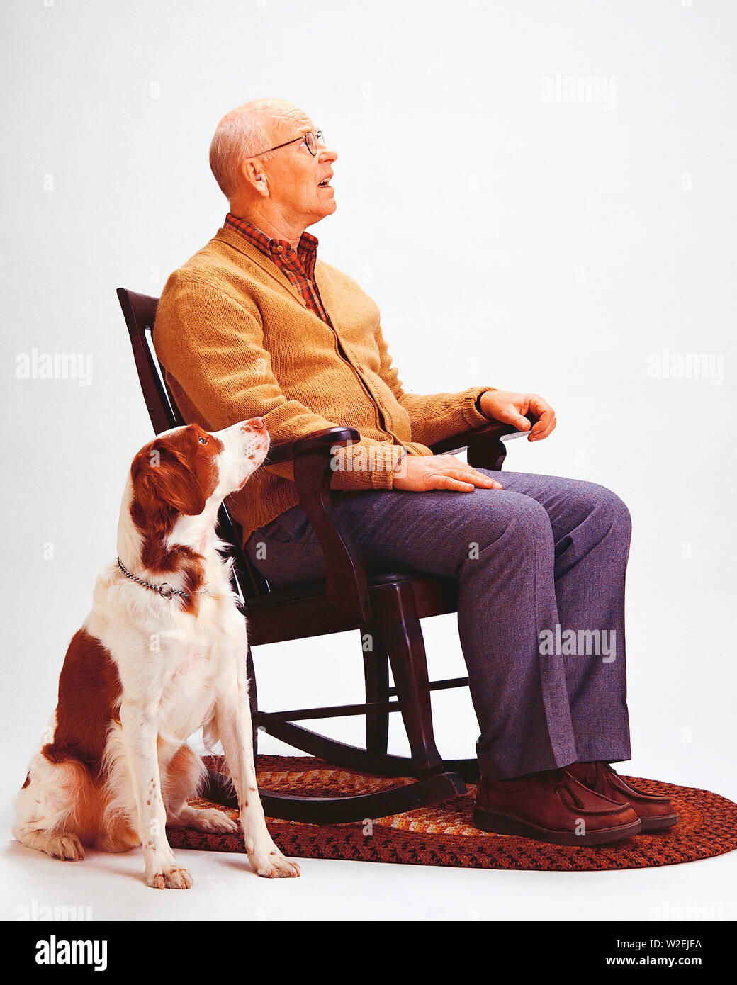 Senior maschile seduto in una sedia a dondolo con un cane accanto a lui sia guardando il cielo Foto Stock