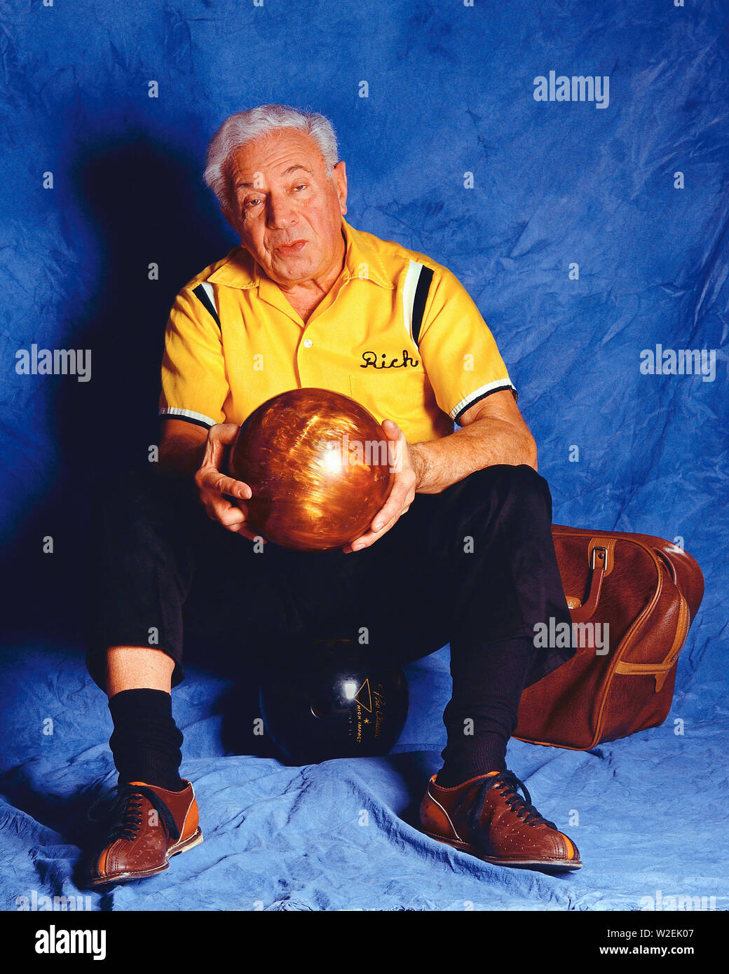 Bowler vecchio seduto su uno sfondo blu tenendo una palla da bowling Foto Stock