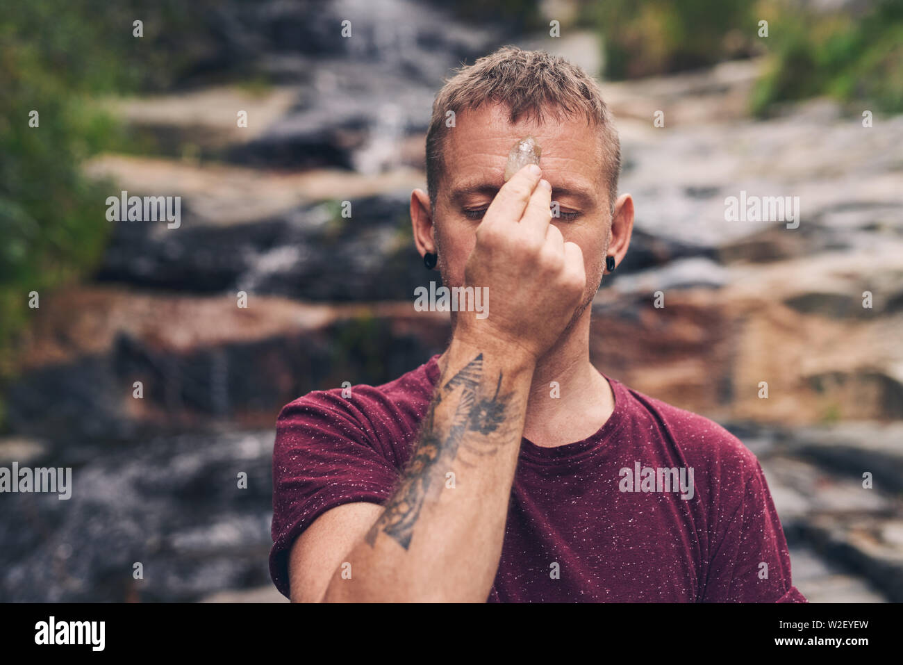Uomo in piedi da una cascata di concentrare sul suo crystal Foto Stock