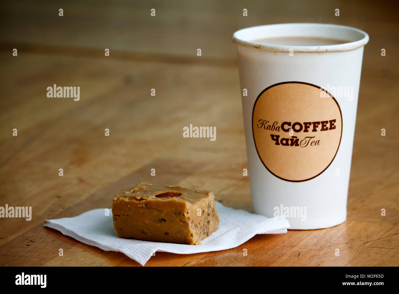 Bicchiere di carta con una iscrizione in ucraino e inglese il tè e il caffè  sono collocati su una superficie di legno, e accanto a un pezzo di dolci  orientali Foto stock -
