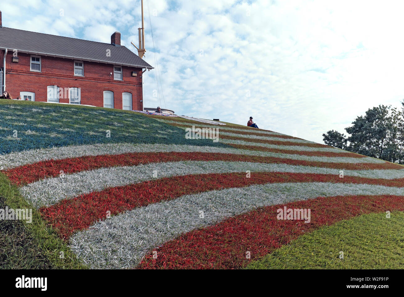 Un gigante di noi bandiera dipinta in erba sul pendio di una collina in Fairport Harbor, Ohio, USA offre poche persone in un punto panoramico per vedere il 2019 fuochi d'artificio. La collina è stata dipinta in onore degli Stati Uniti il 4 luglio di vacanza durante la quale Fairport porto sul Lago Erie ospita un evento in più giorni che culminano nella serata del 7 luglio con uno spettacolo di fuochi d'artificio. Foto Stock