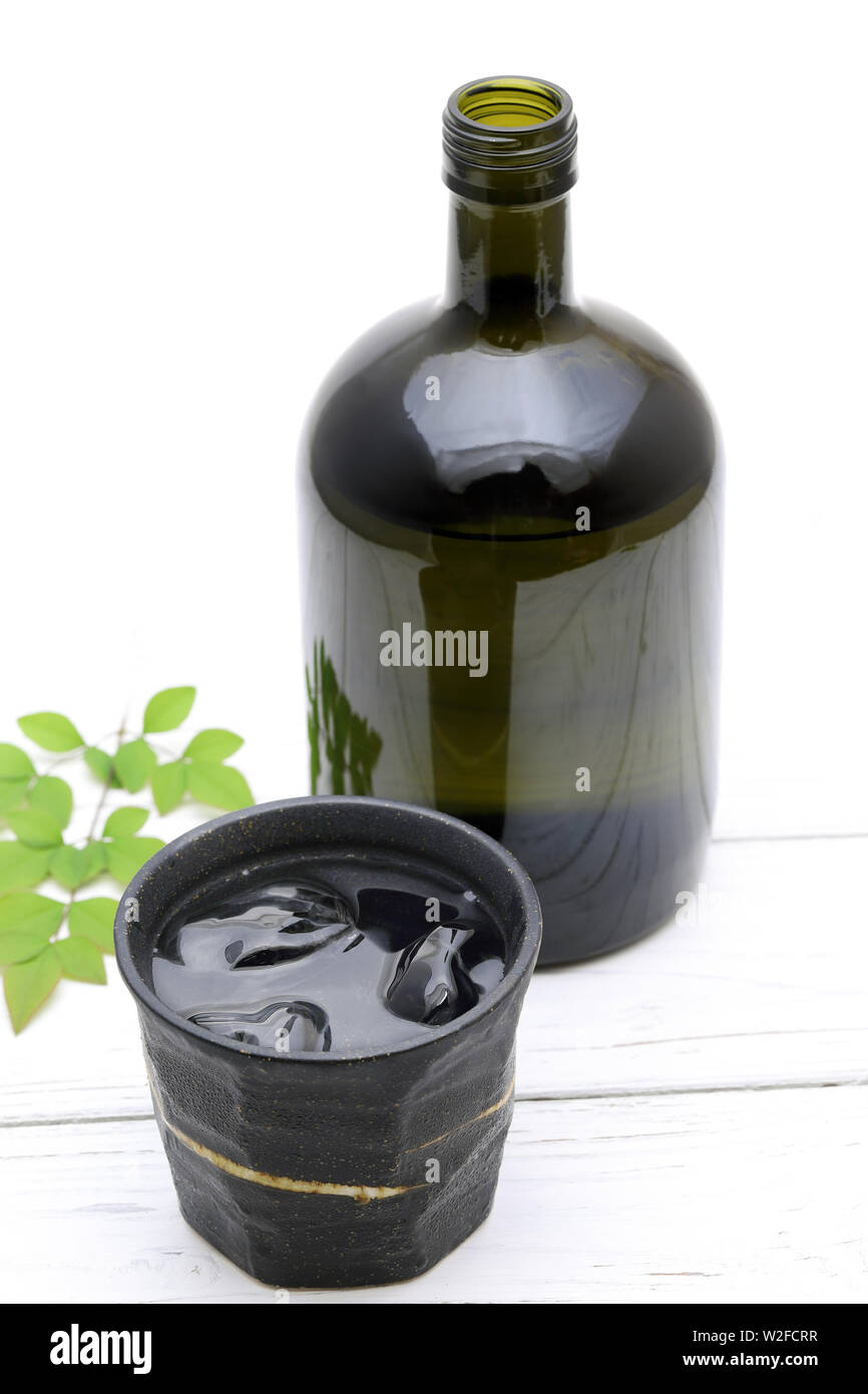 Bottiglia di shochu giapponese e la ciotola in ceramica su legno tavolo bianco Foto Stock