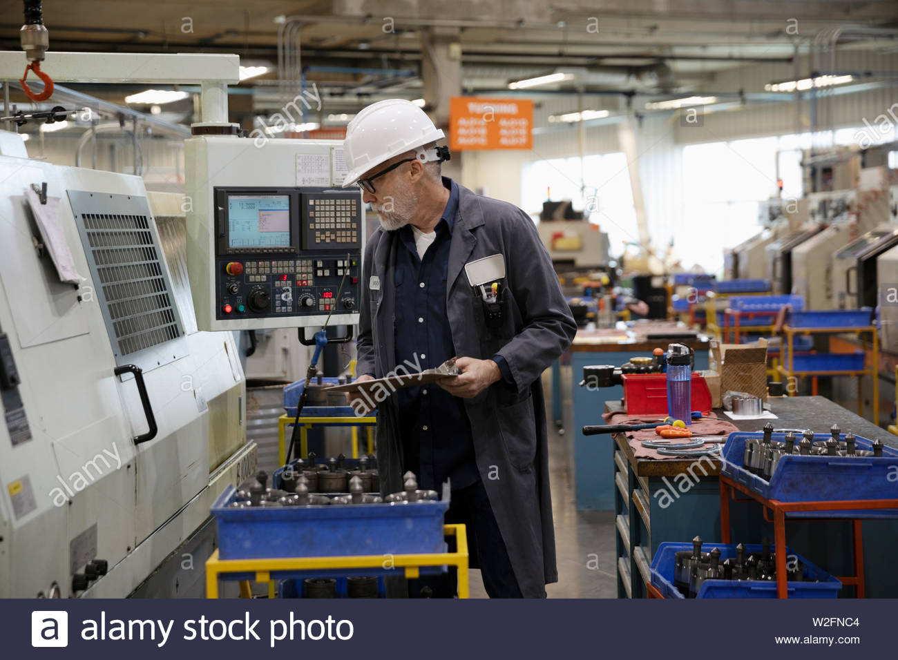 Machine shop supervisor esaminare le attrezzature sul pavimento di fabbrica Foto Stock