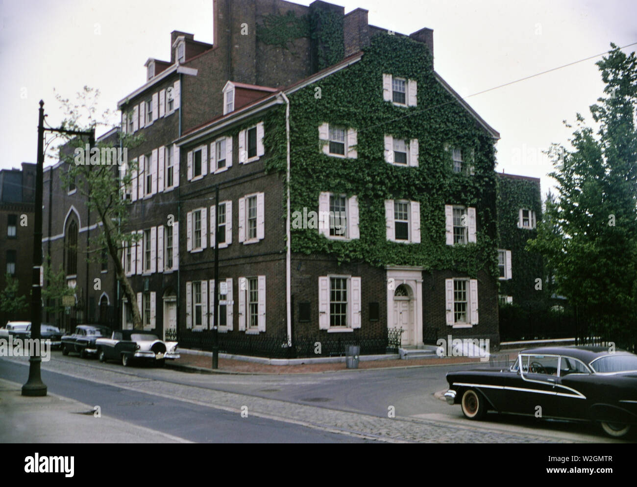 Auto parcheggiate in strada di fronte a un vecchio edificio in una città americana ricoperti di edera verde ca. 1961 Foto Stock