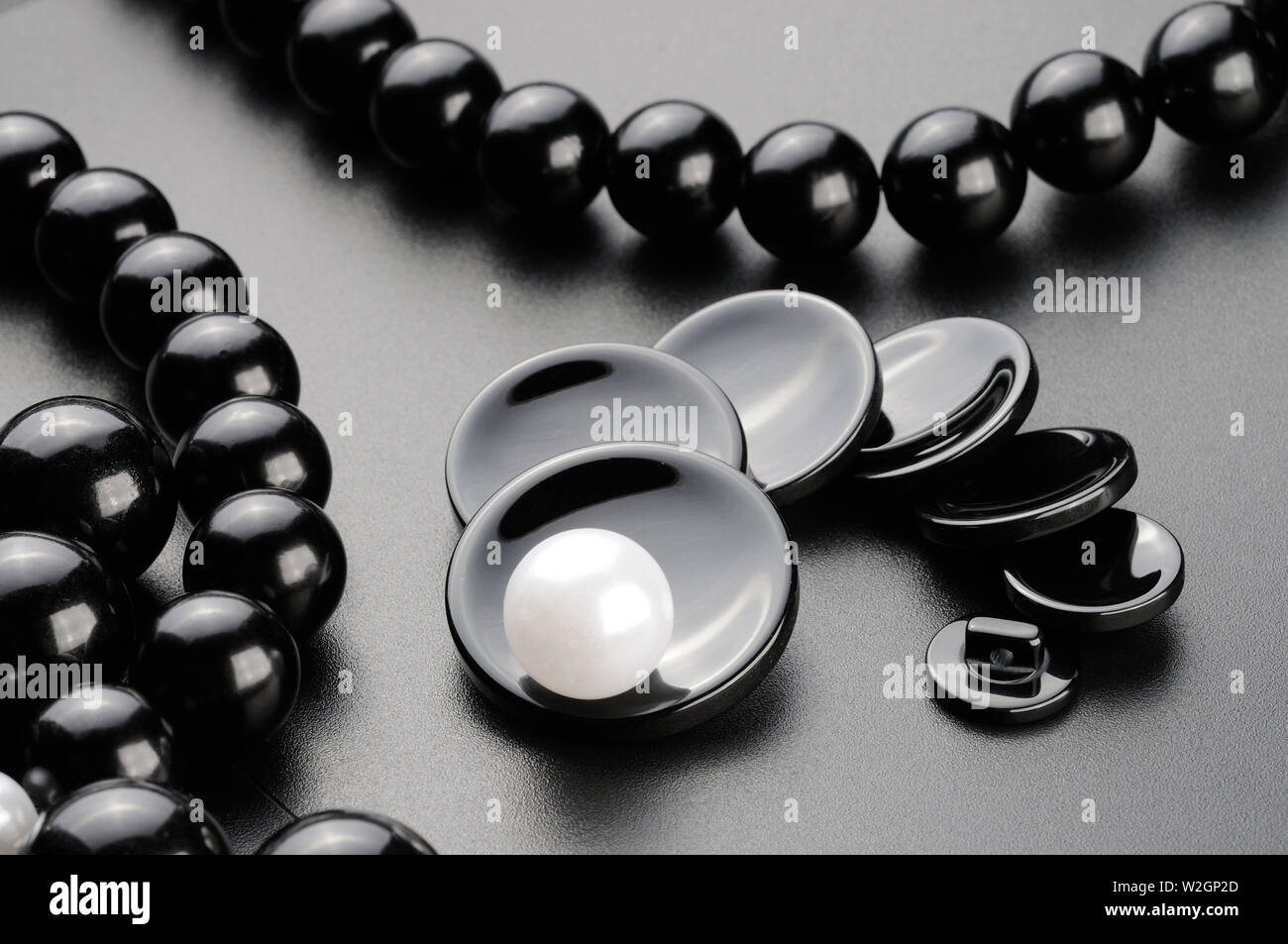 Pulsanti di cucitura e perle sulla superficie nera. Concetto unico Foto Stock