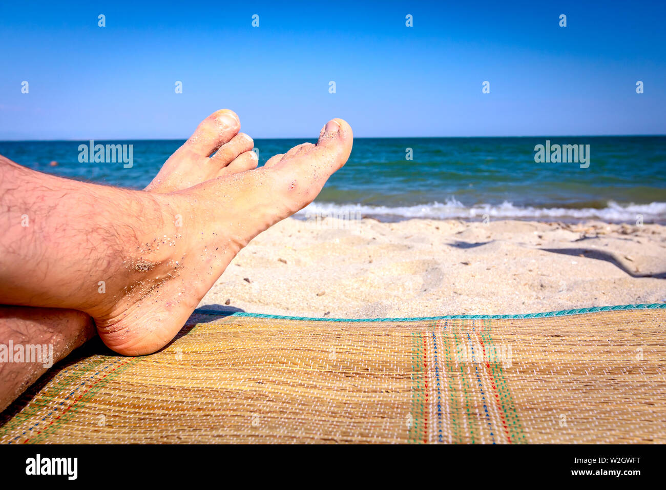 L uomo per le gambe fino a quando non viene a prendere il sole in giacente spensierato sul tappeto accanto alla linea di costa, sulla spiaggia pubblica. Foto Stock