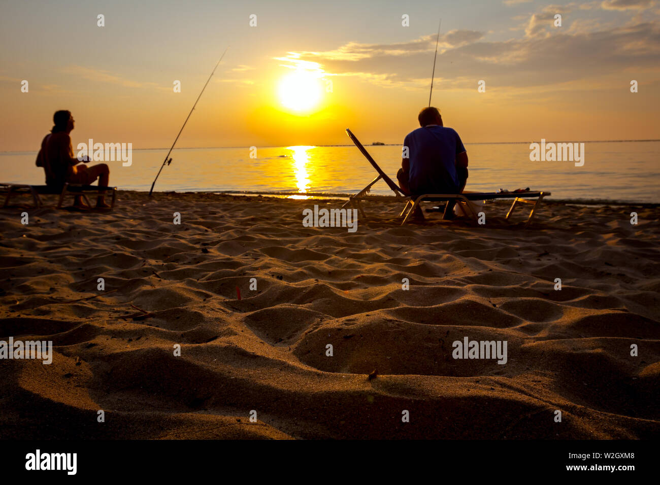 Due amici sono la cattura del pesce da una spiaggia di sabbia con canne da pesca, sunrise mattina oltre il mare Mediterraneo. Foto Stock
