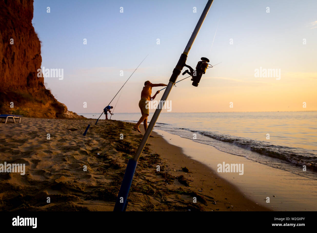 Due amici sono la cattura del pesce da una spiaggia di sabbia con un paio di canne da pesca, mattina oltre il mare Mediterraneo. Foto Stock