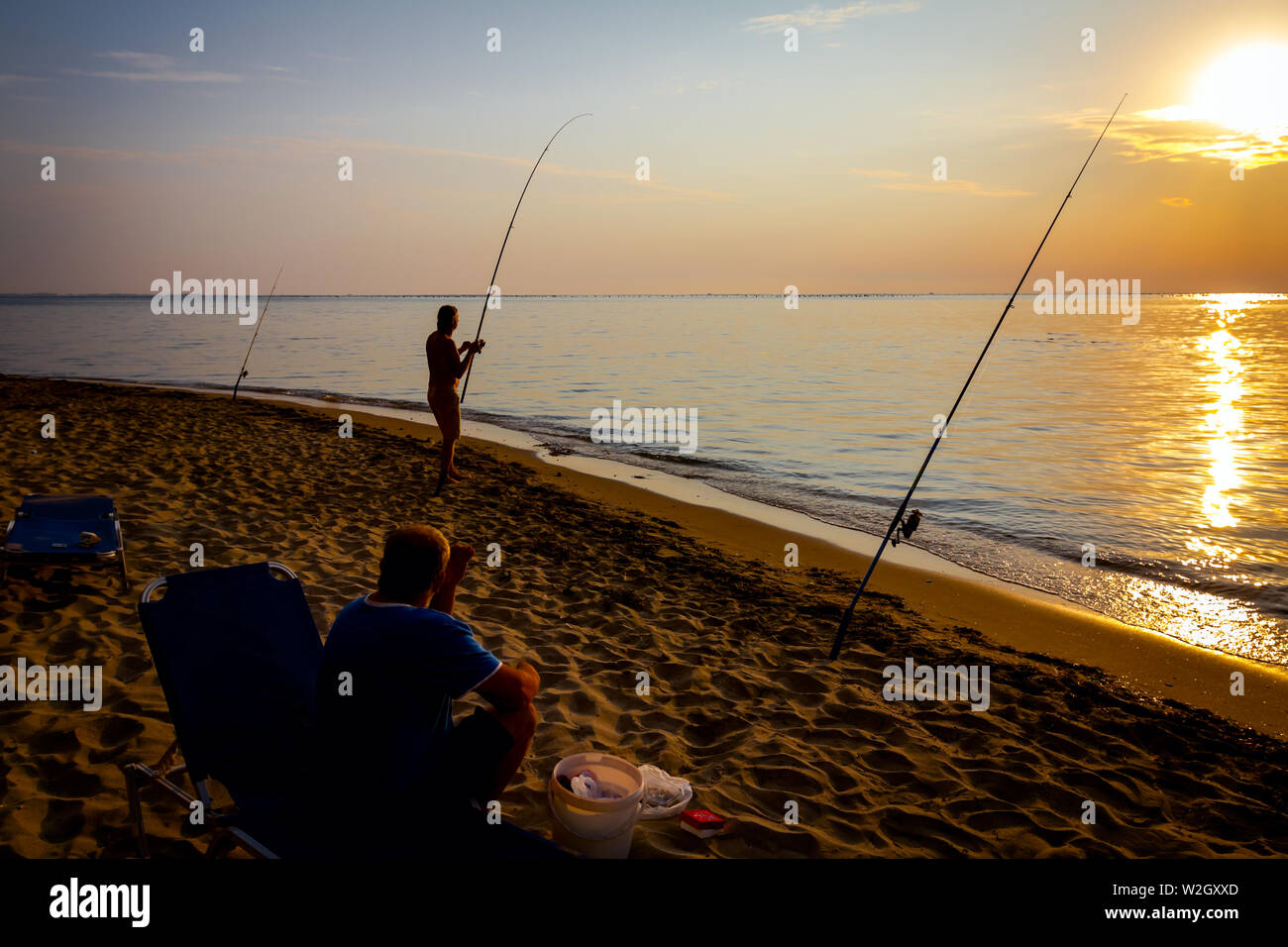 Due amici sono la cattura del pesce da una spiaggia di sabbia con canne da pesca, sunrise mattina oltre il mare Mediterraneo. Foto Stock